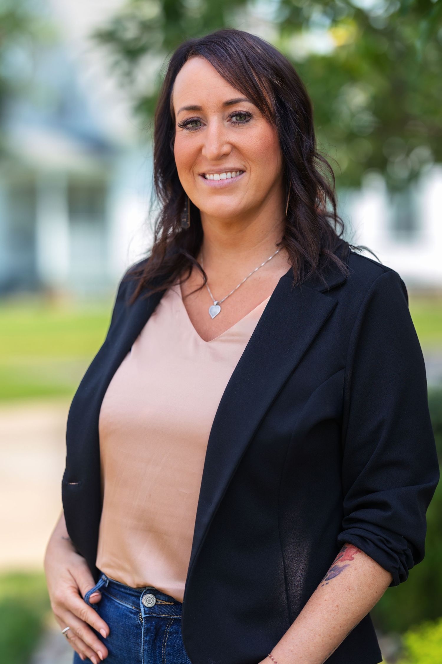 Professional outdoor portrait of person in black blazer and beige top with natural lighting.