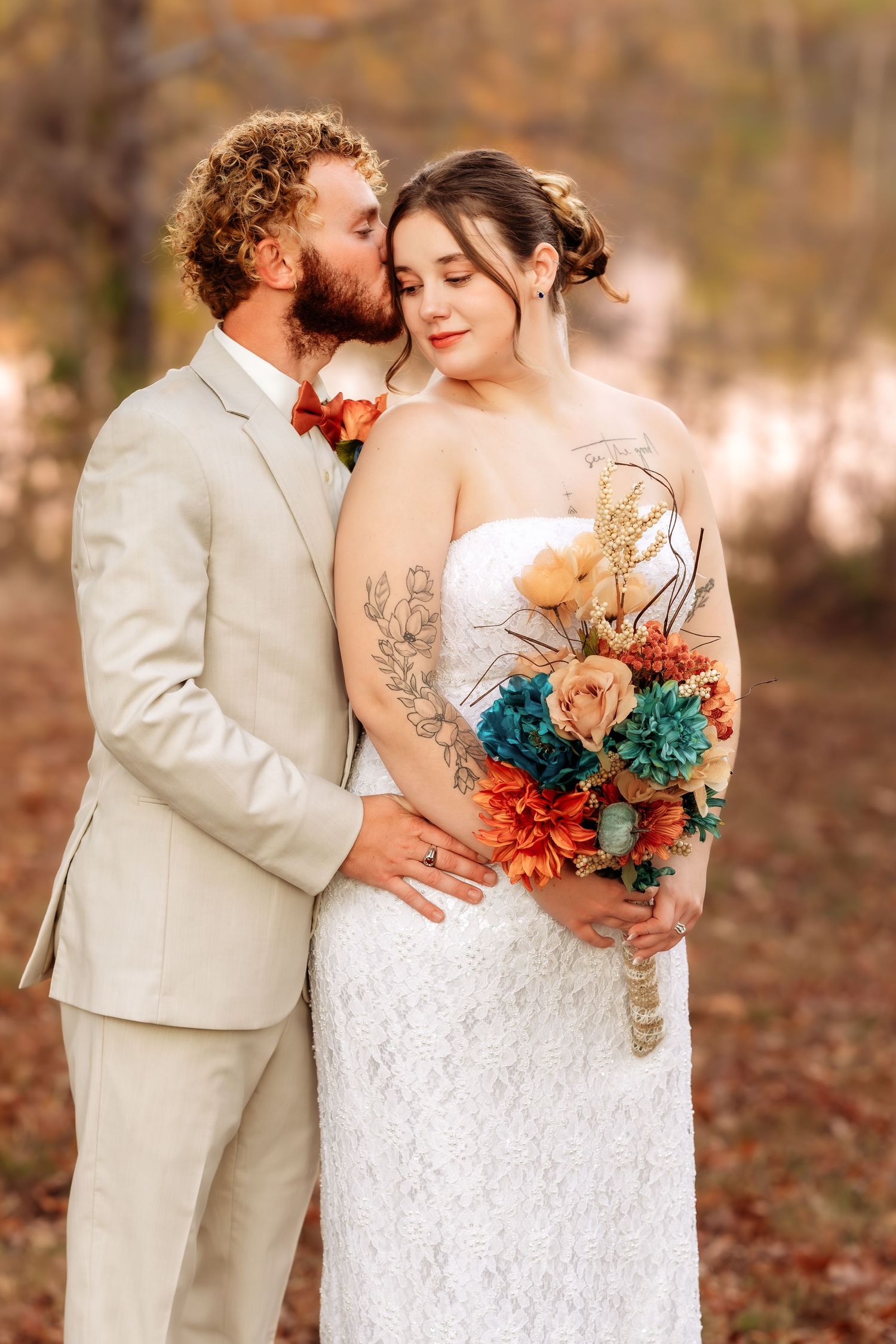 Romantic autumn wedding portrait with couple embracing, featuring a white lace gown and cream-colored suit.