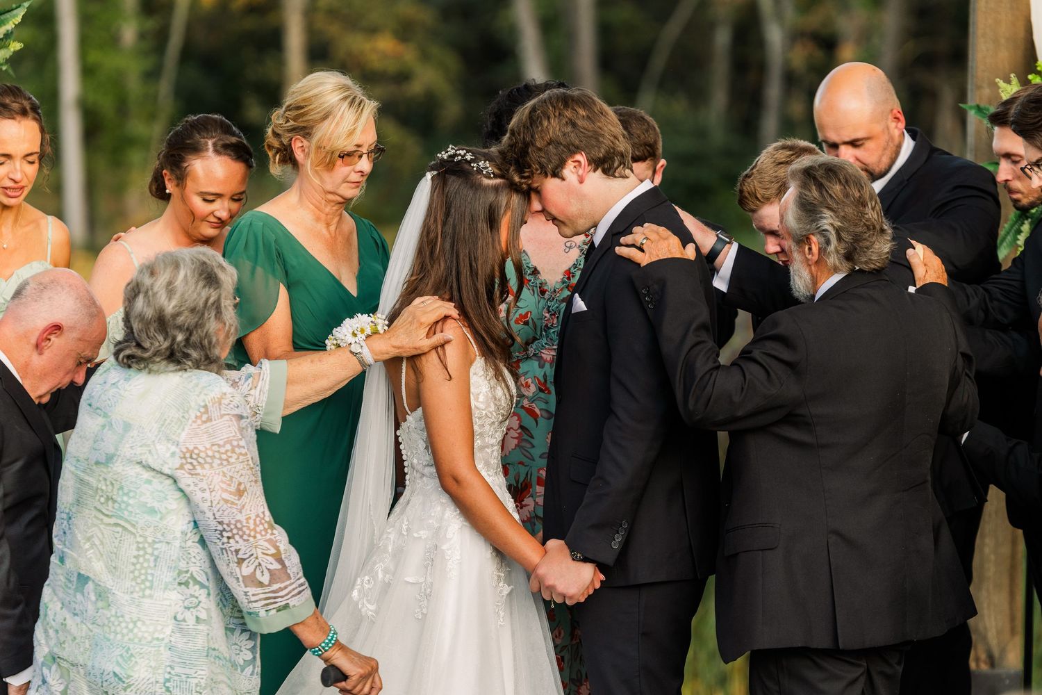 Wedding guests praying over the bride and groom during emotional outdoor celebration.