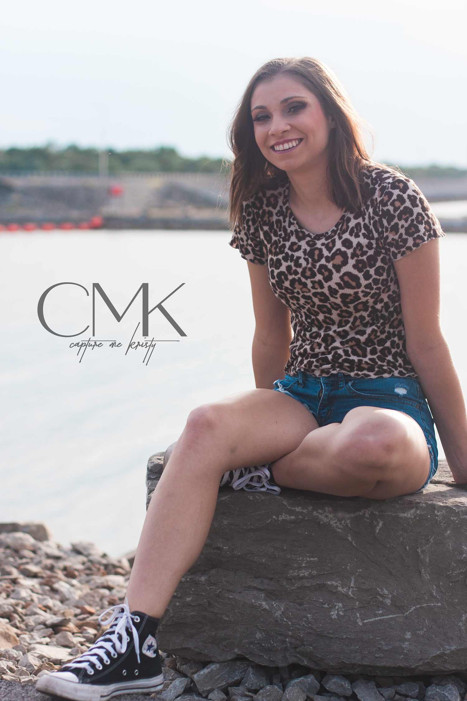 Casual outdoor portrait showing subject sitting on rock wearing animal print top and denim shorts.
