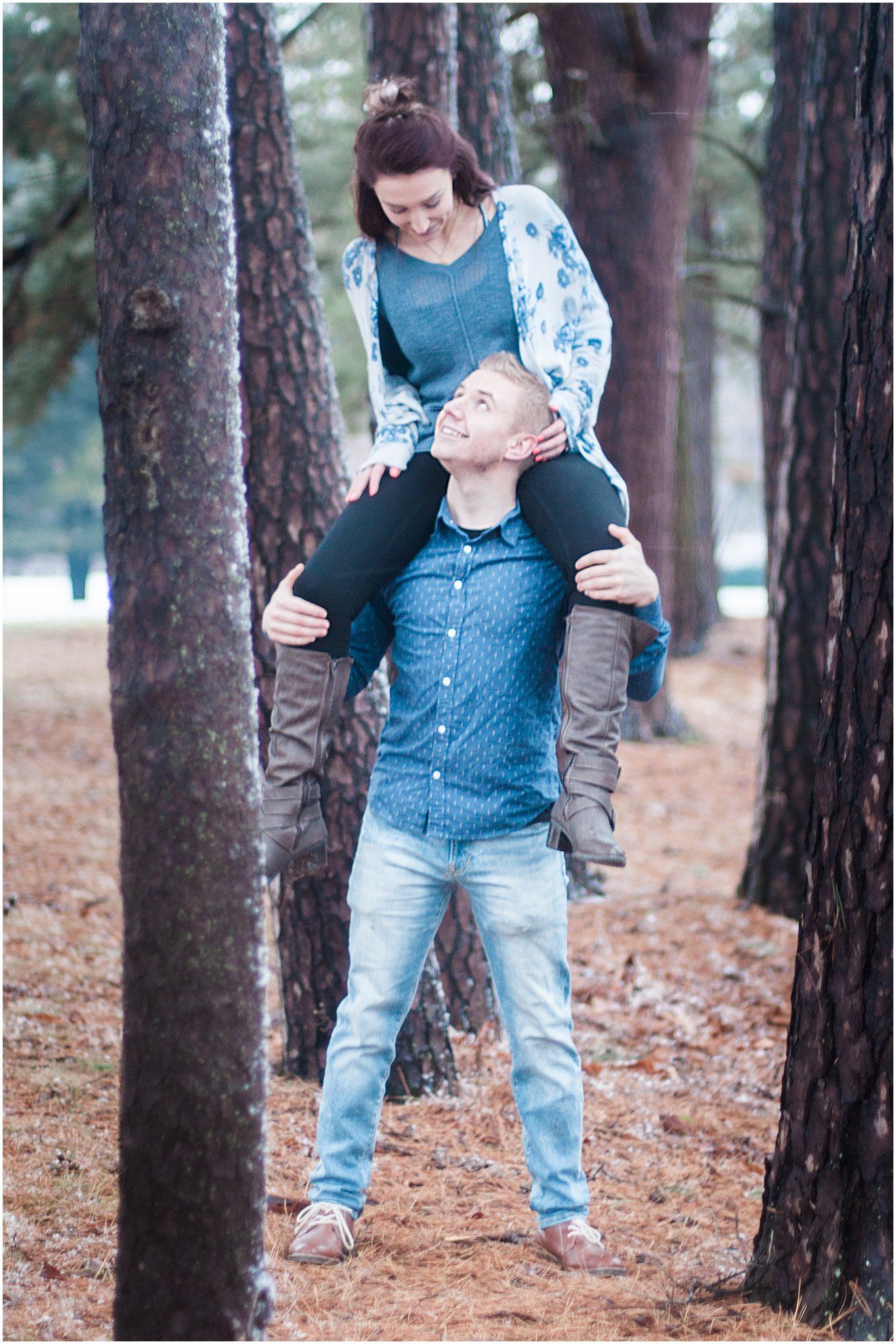 Couple enjoying a playful piggyback ride moment among tall pine trees.