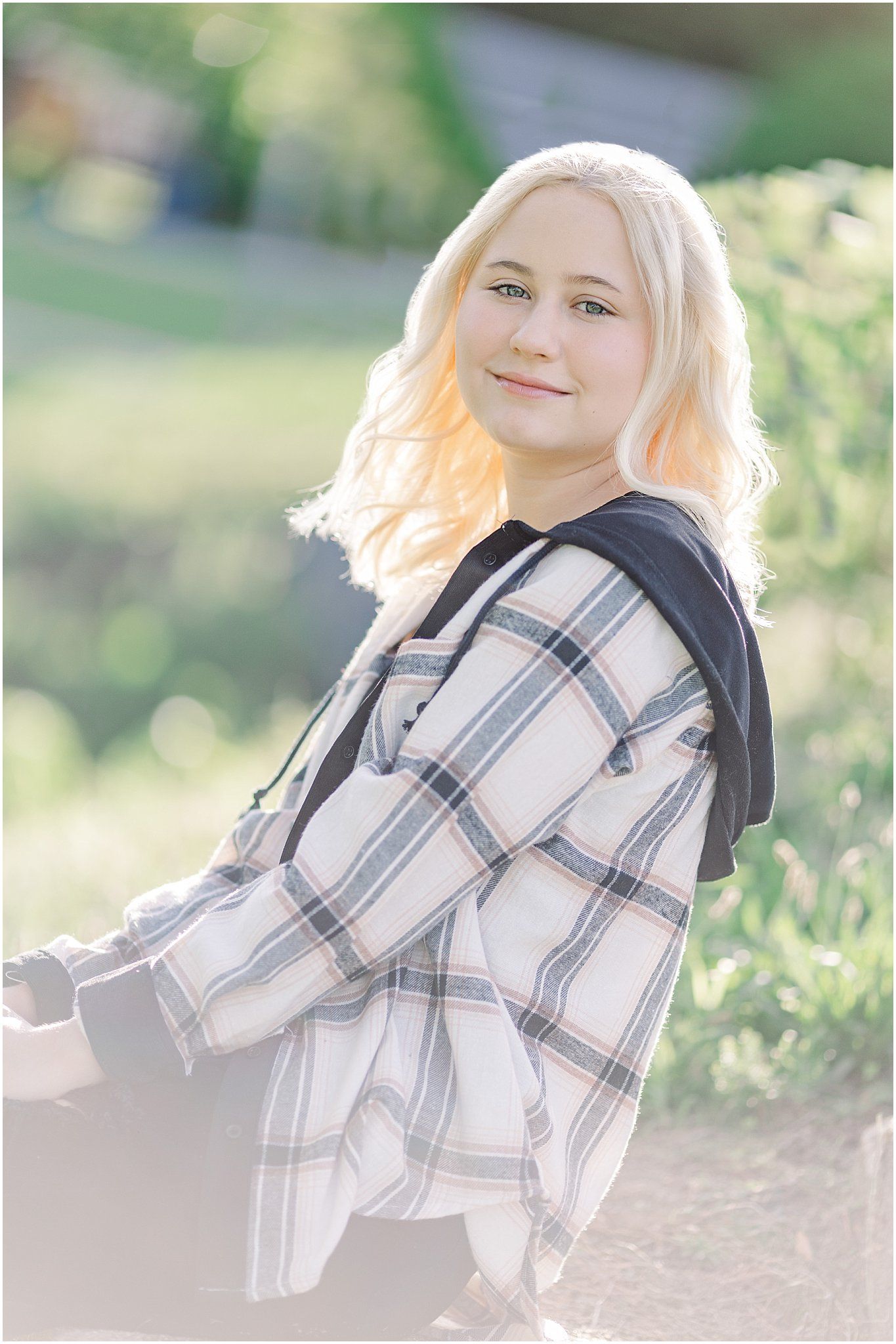 Senior girl leaning back holding knees while sitting on step with backlit hair