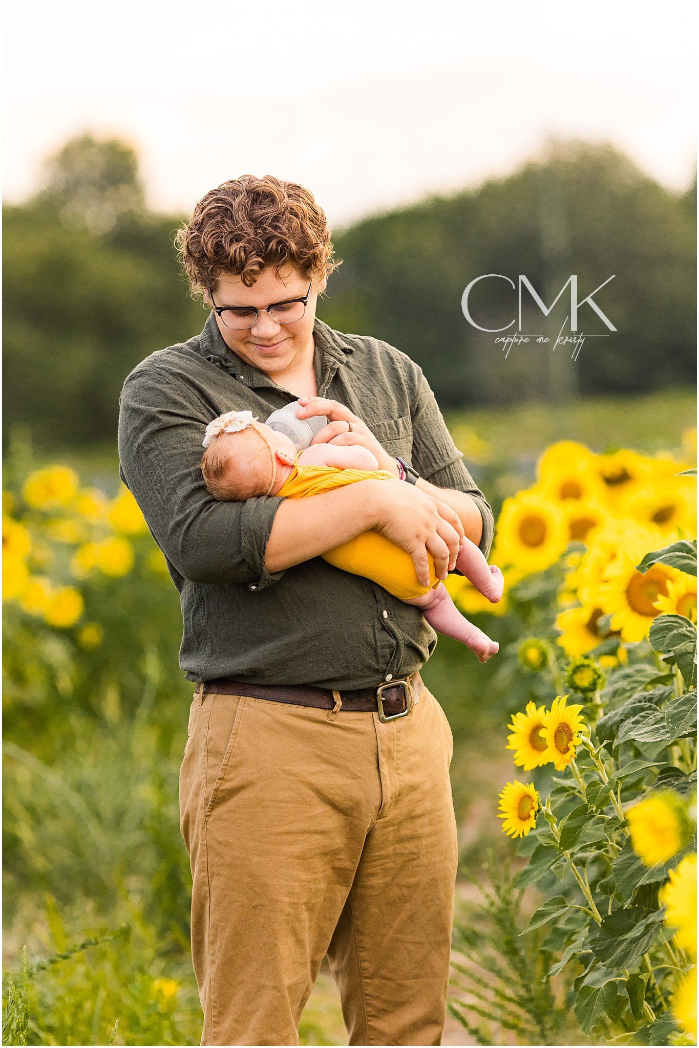 A heartwarming moment between parent and infant in a field of bright sunflowers.