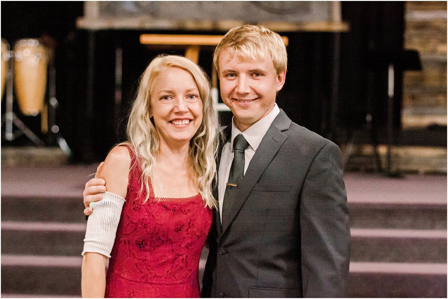 A couple in formal attire poses together at a rustic wedding venue.