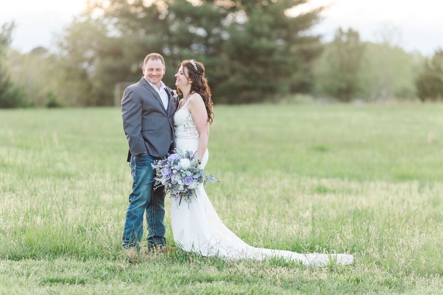 Romantic wedding portrait of couple in green field with flowing white dress and blue bouquet.