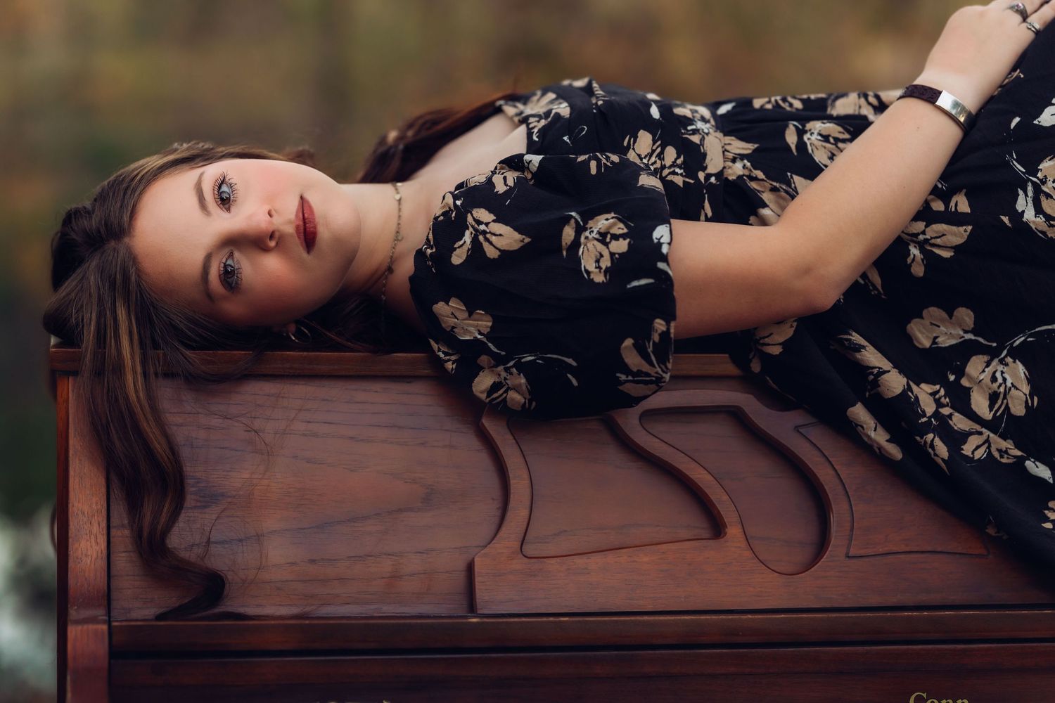 Artistic portrait on wooden piano in floral dress with natural lighting.