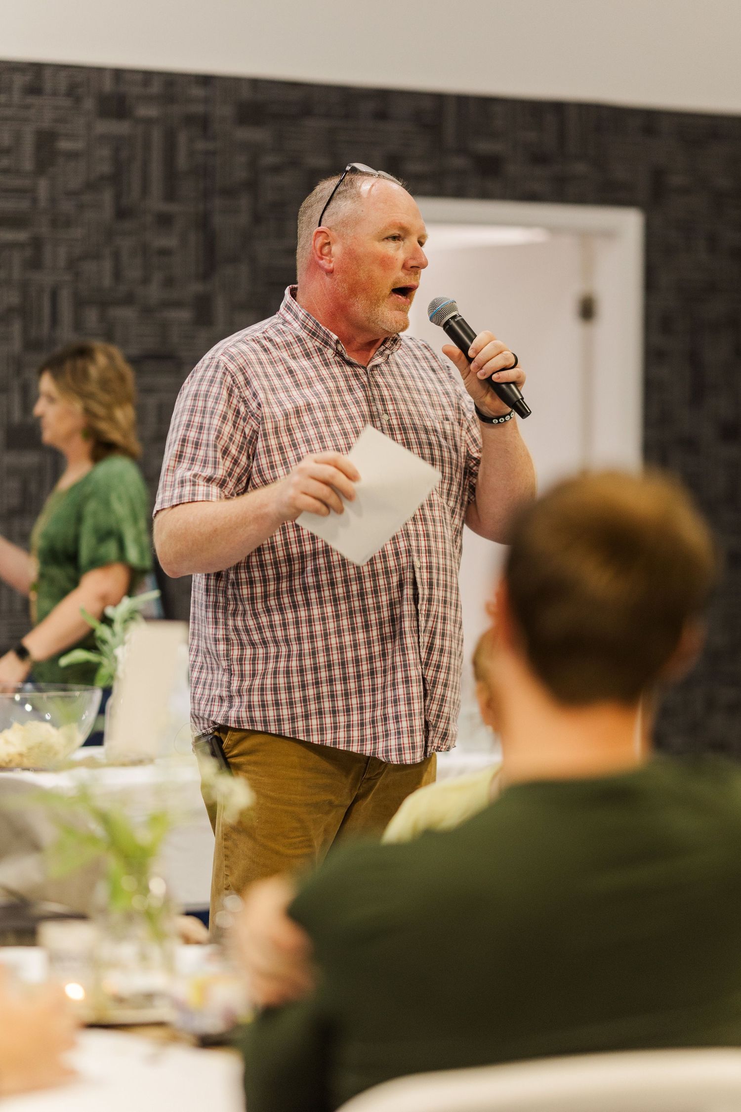 Speaker addressing audience during indoor event with dark textured walls.