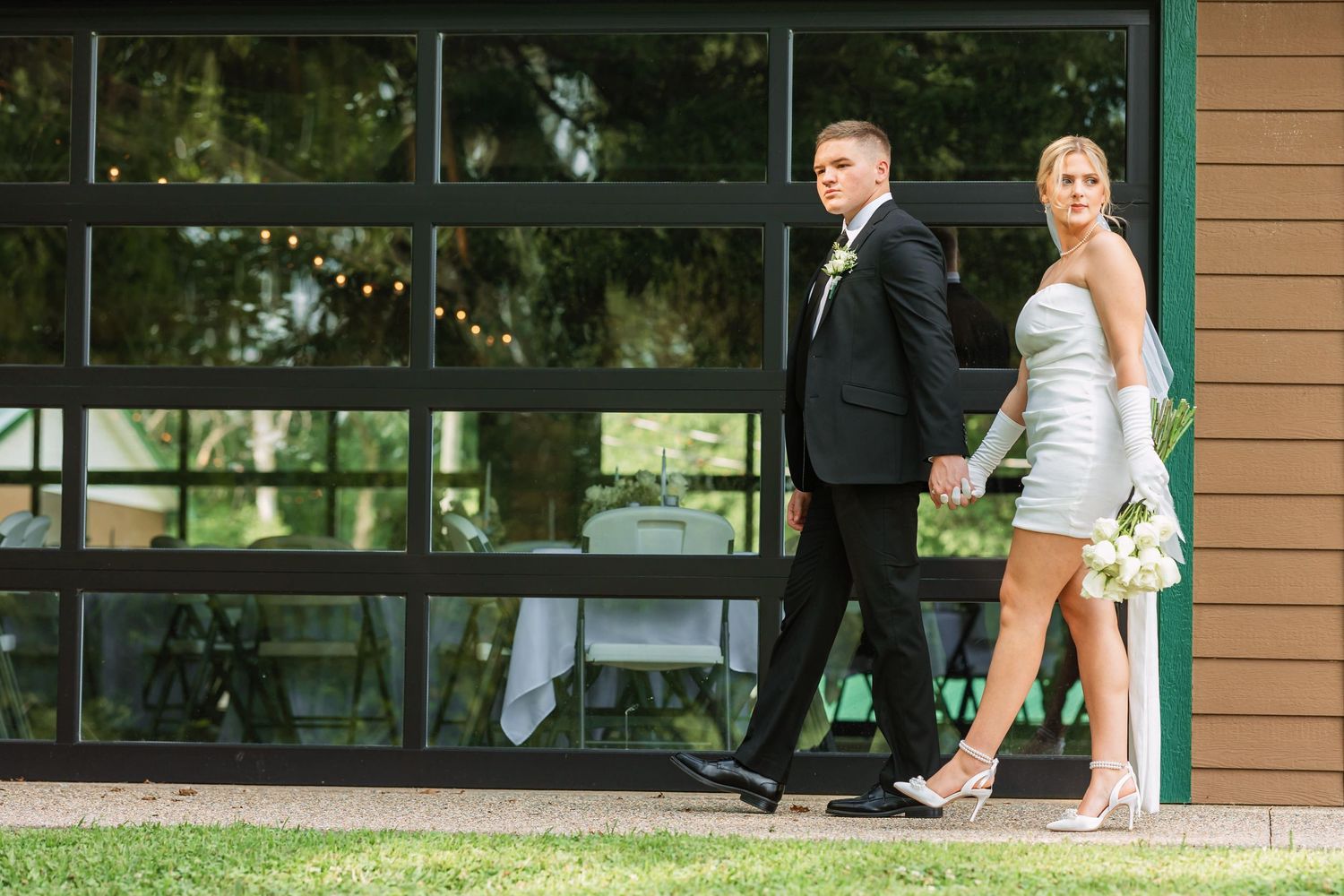 Wedding couple sharing playful moments outside modern building with glass windows.