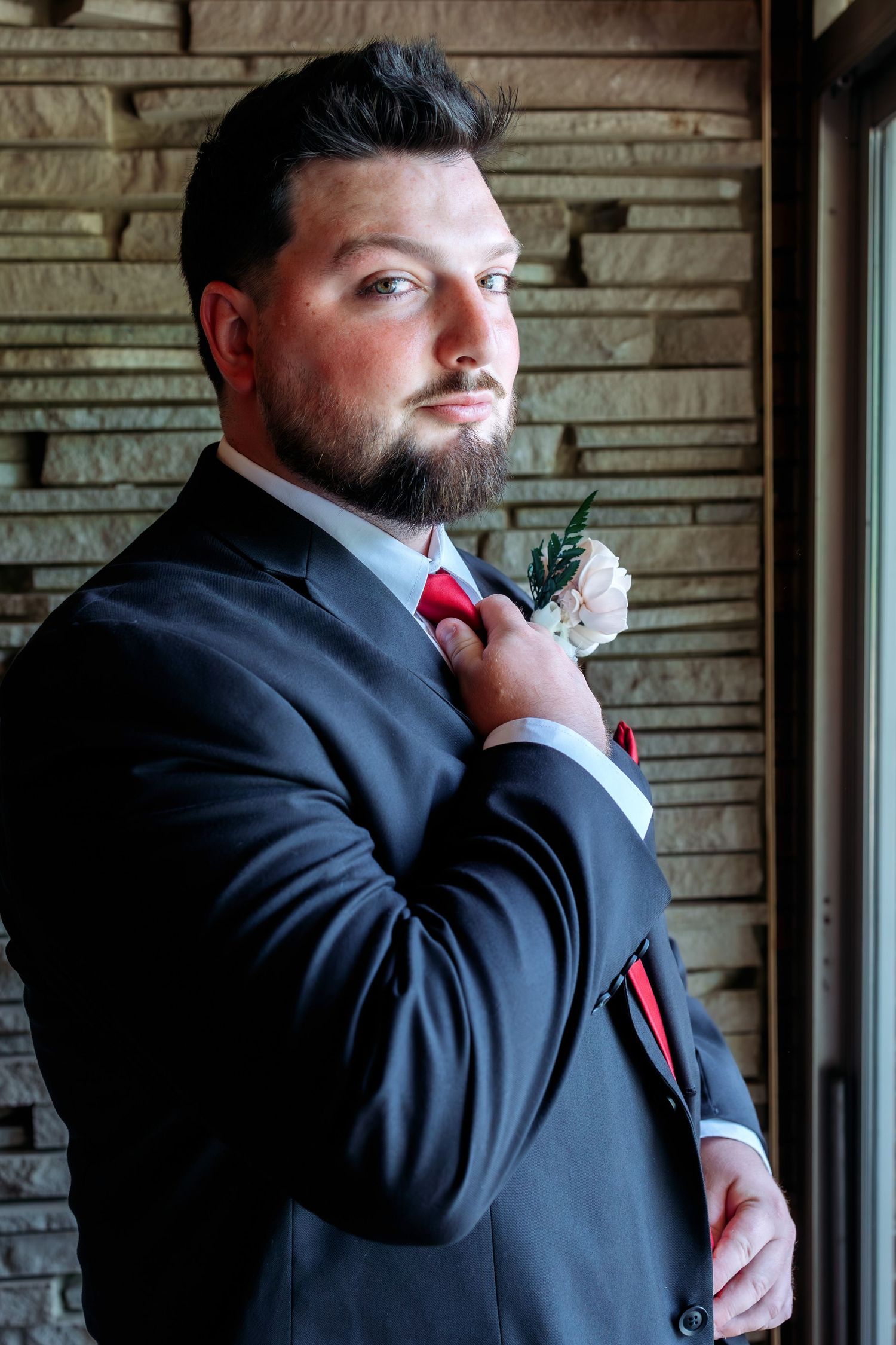 Groom in classic black tuxedo adjusts tie in dramatic portrait.