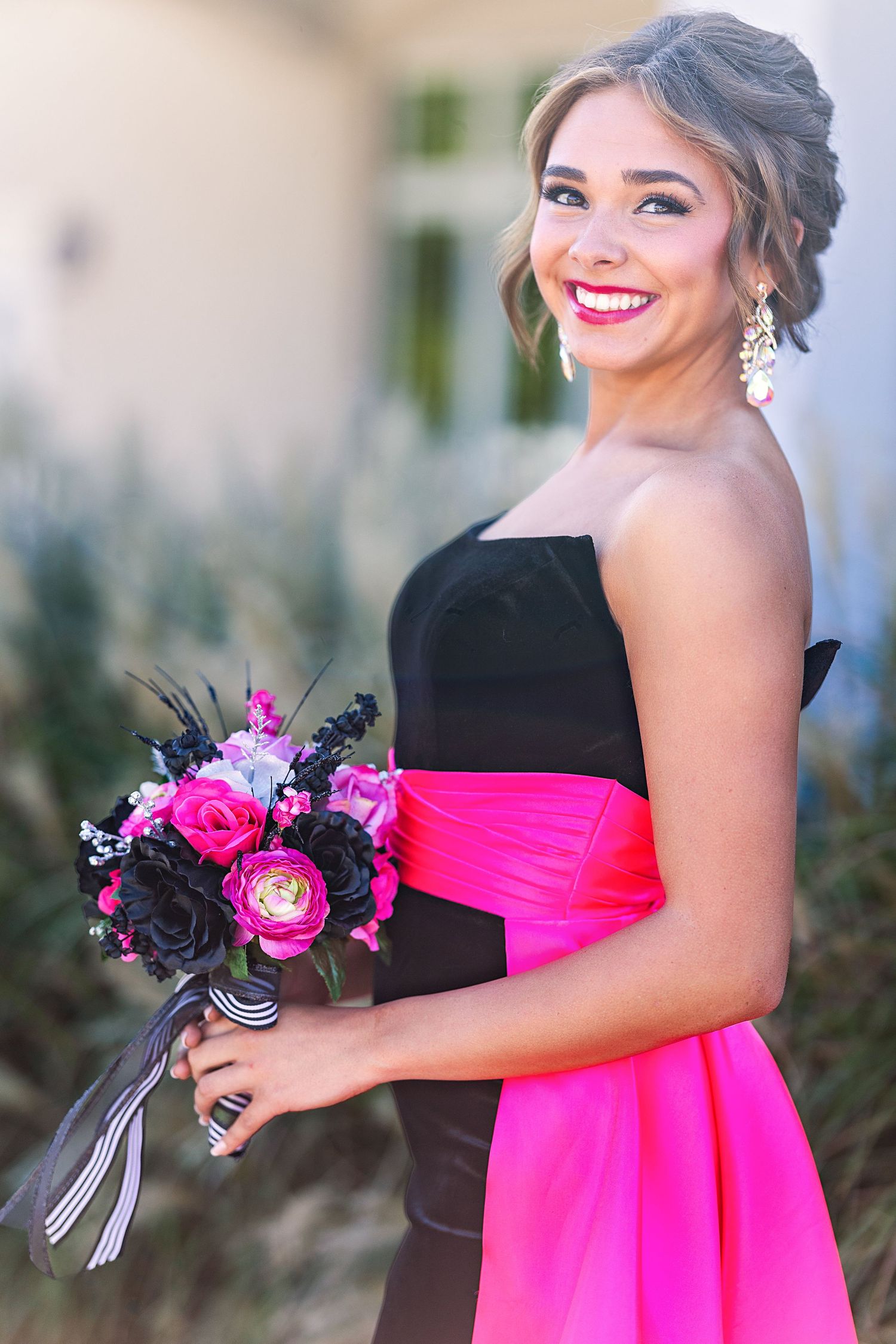 A portrait of someone in a black and pink formal dress holding a vibrant bouquet with a bright smile.