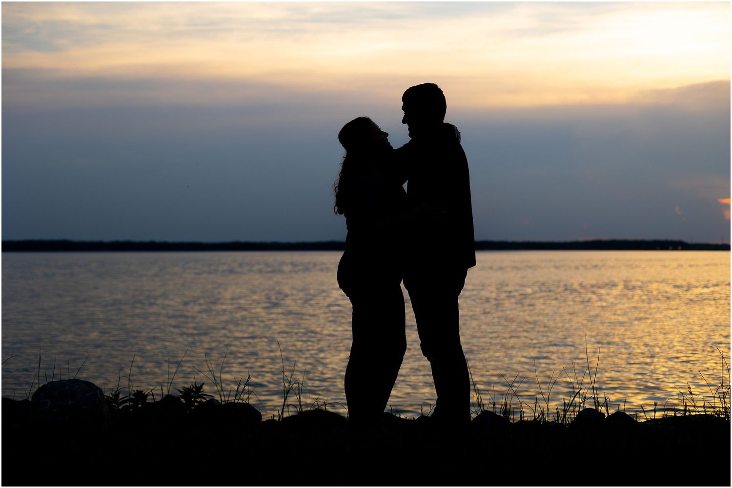 Silhouette of a couple standing together against a sunset sky over water.