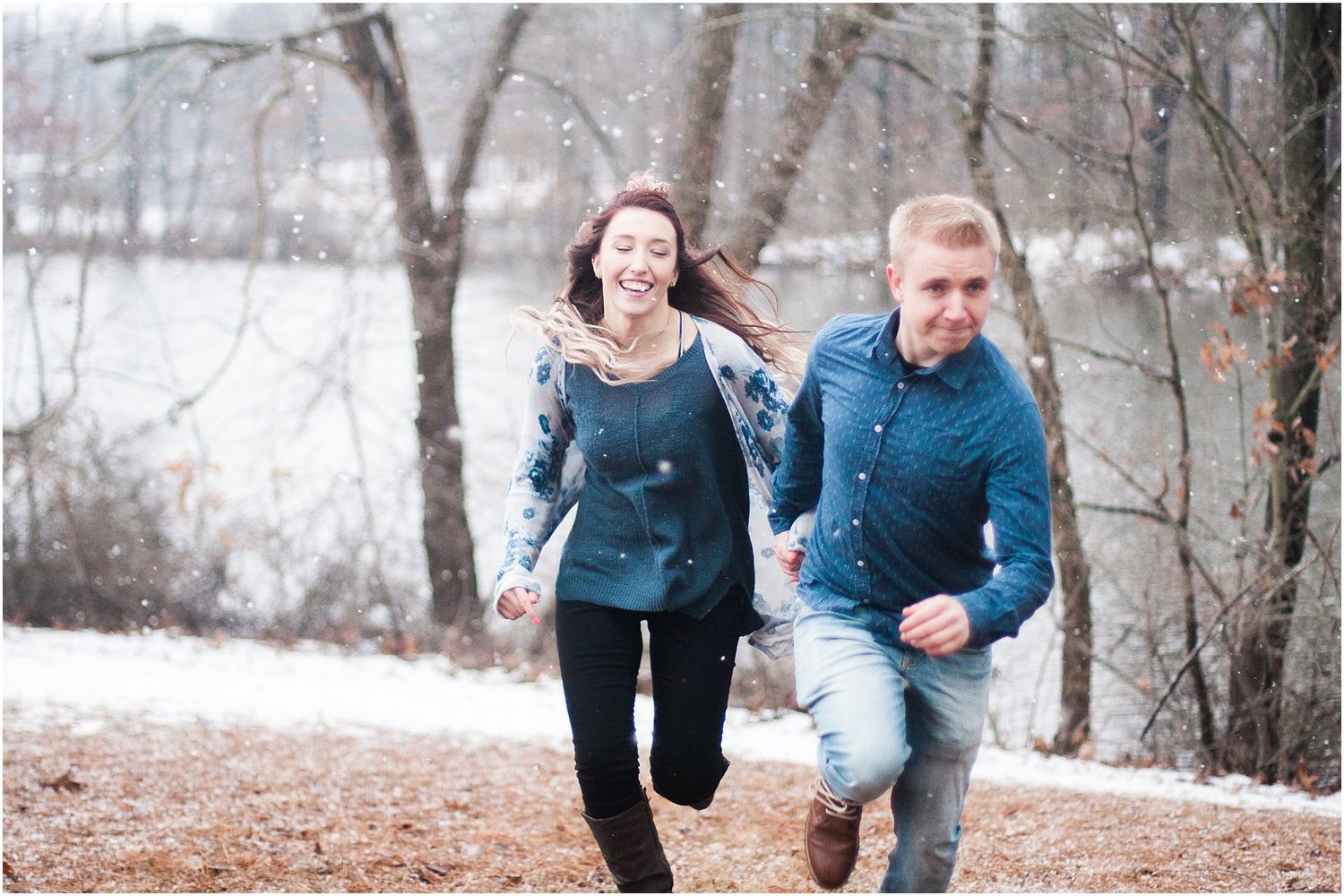 A couple runs together along a snowy trail by the water's edge.