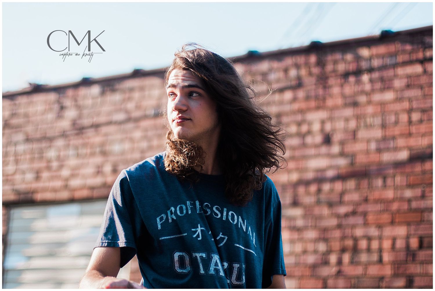 Person in professional otaku shirt with windblown hair against brick wall.