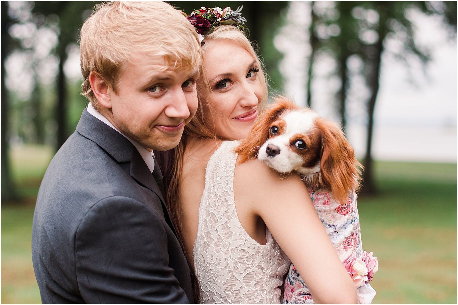 A couple poses with their Cavalier King Charles Spaniel for wedding photos outdoors.