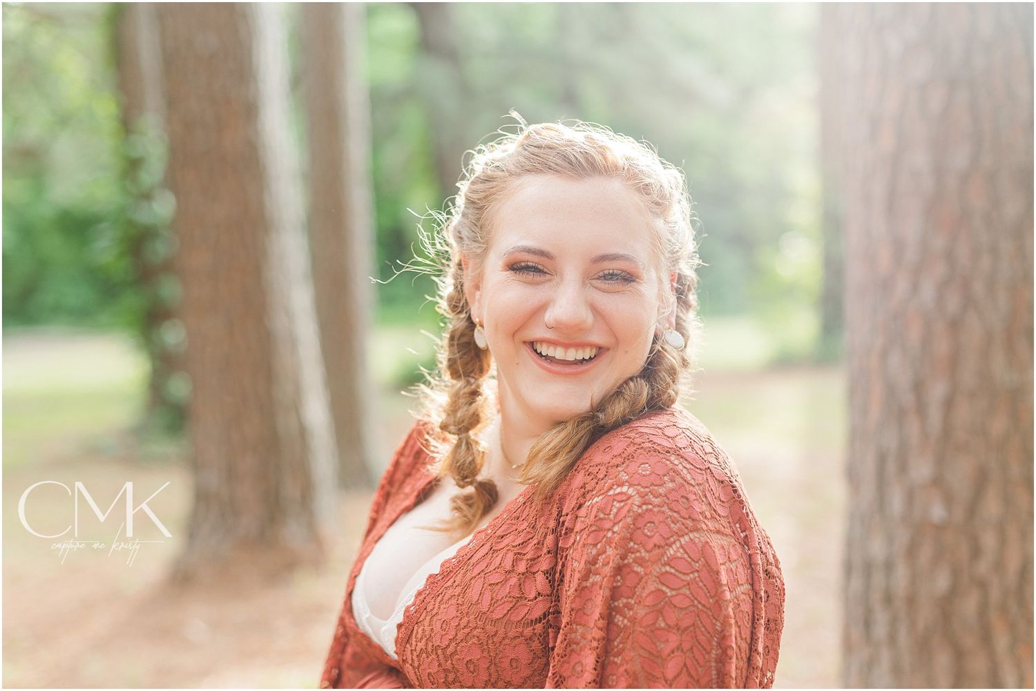 A maternity photoshoot in a forest setting featuring a rust-colored lace dress and braided hairstyle.