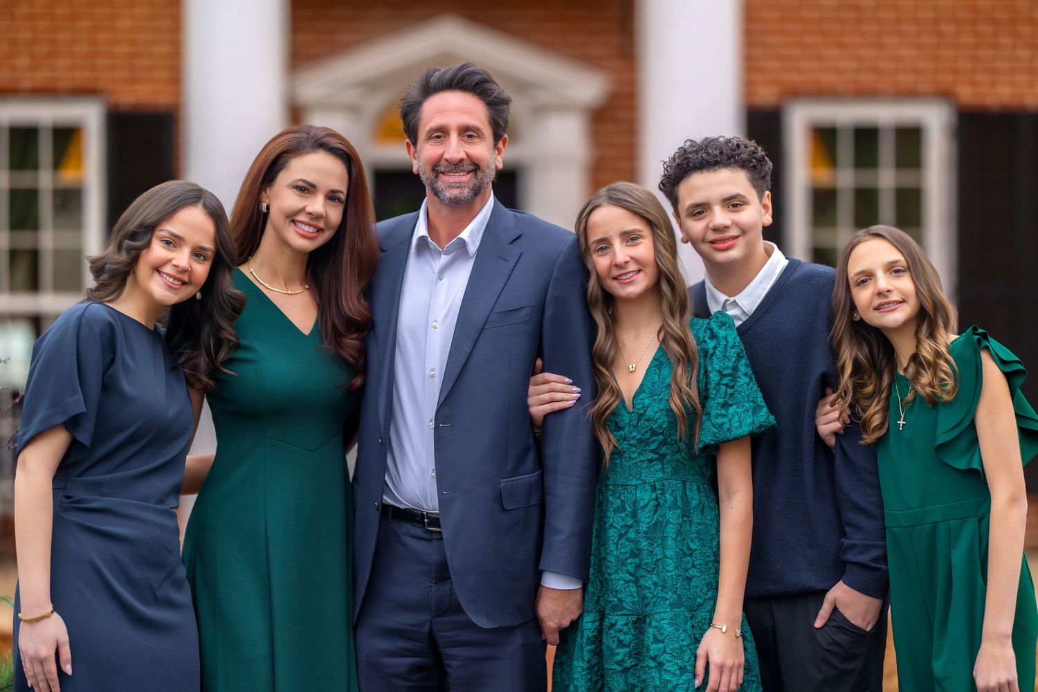 Group photo in formal attire with navy and emerald green dresses outside brick building.