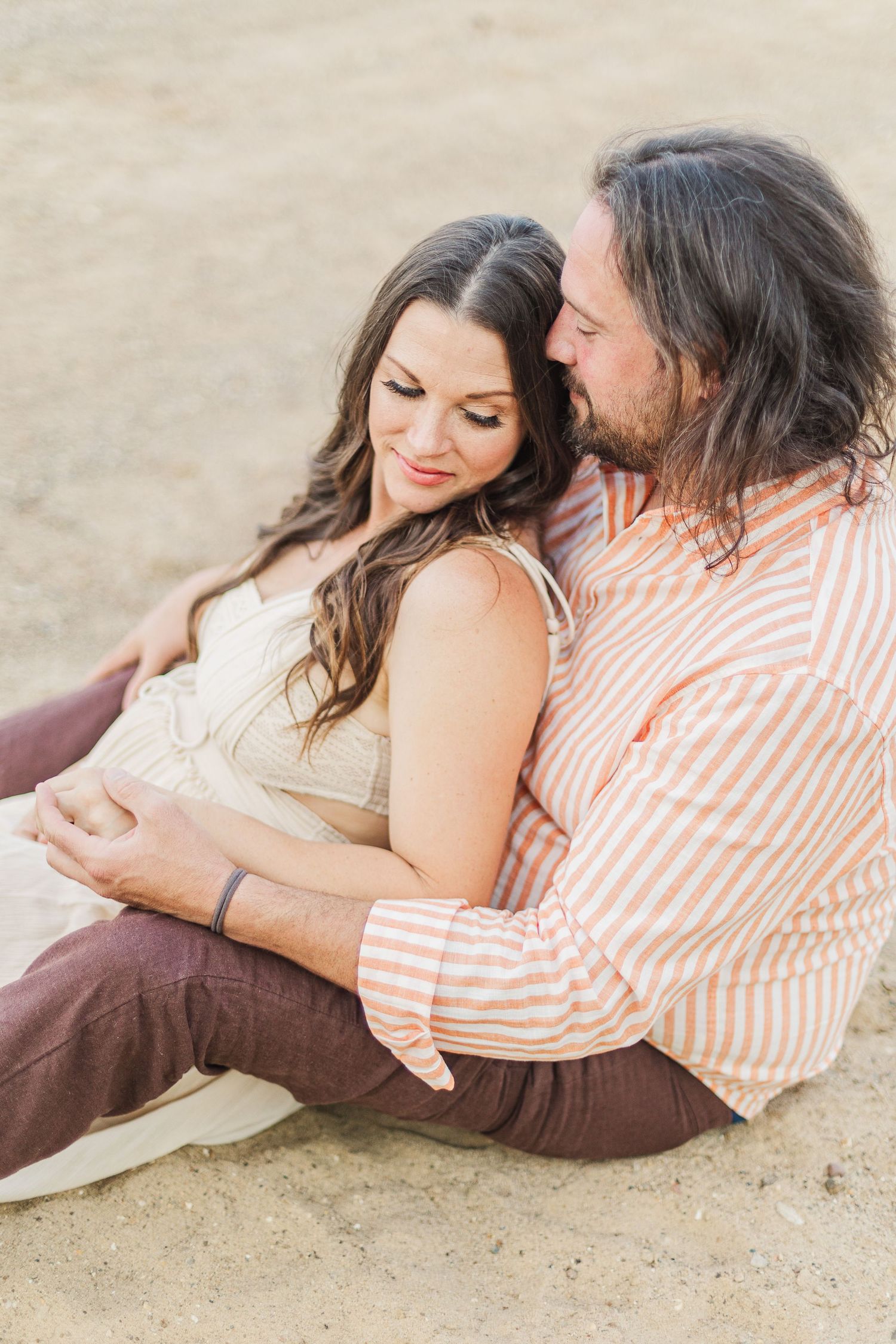 Couple relaxes together on sandy beach in casual attire.
