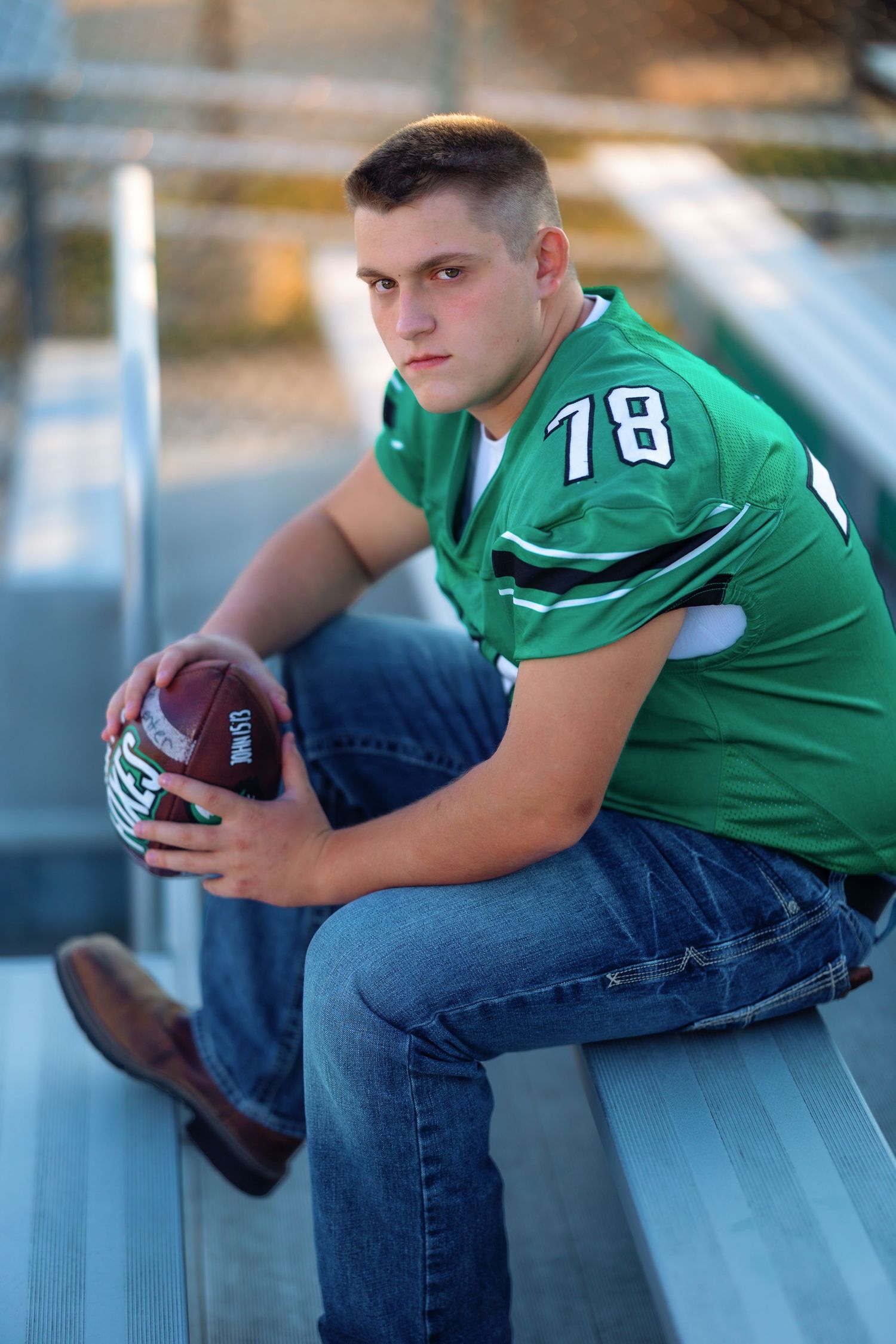 Football player in green jersey sitting on bleachers holding ball.
