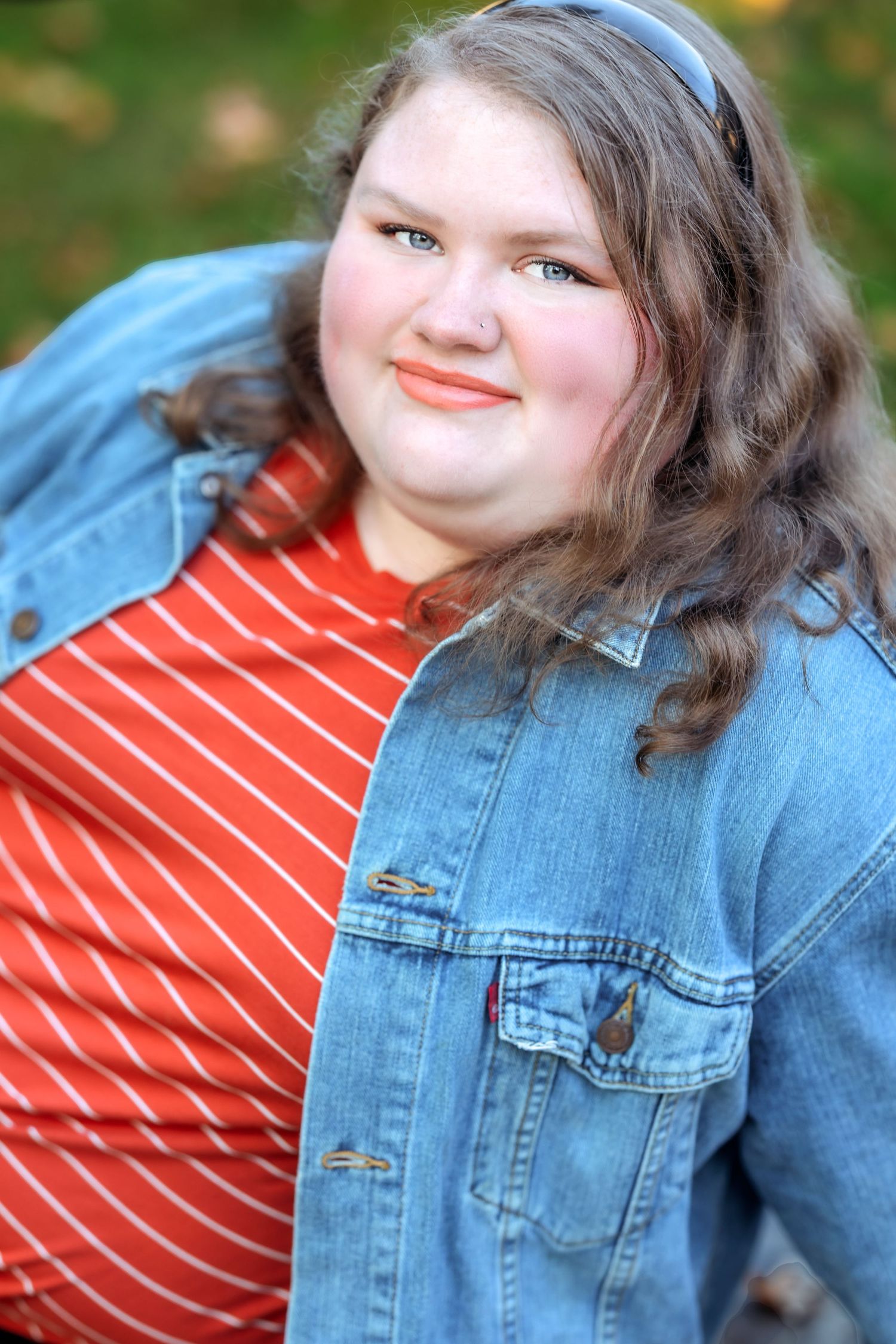 Person wearing orange striped shirt and denim jacket poses outdoors.