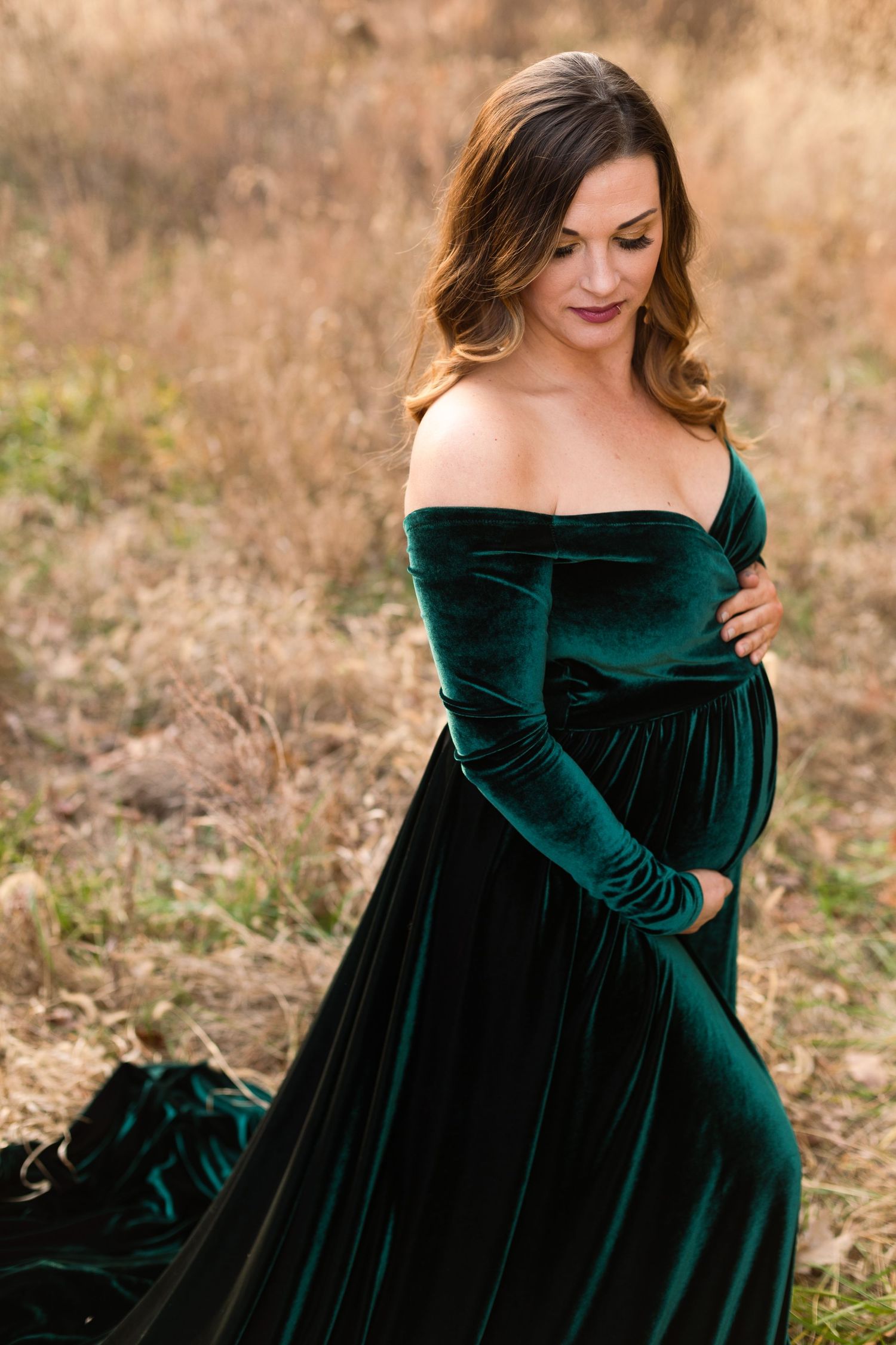 Elegant maternity photo featuring emerald velvet dress against autumn landscape.