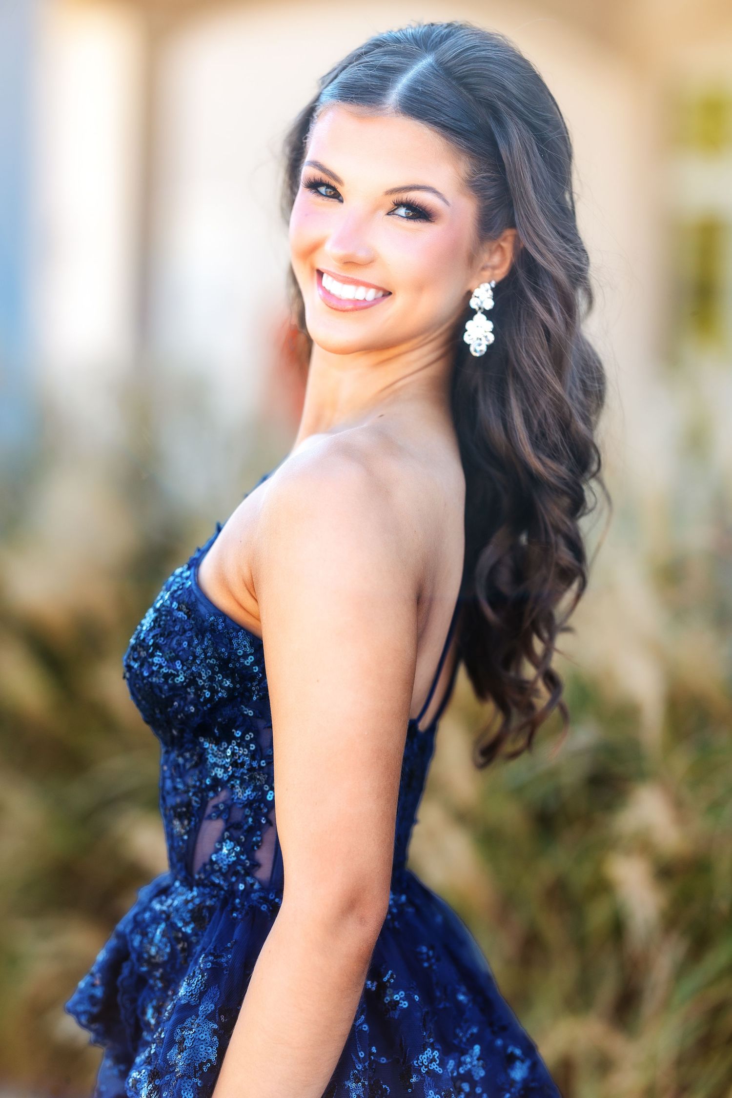 Portrait of someone in a sparkling navy blue gown with elegant hair and jewelry.