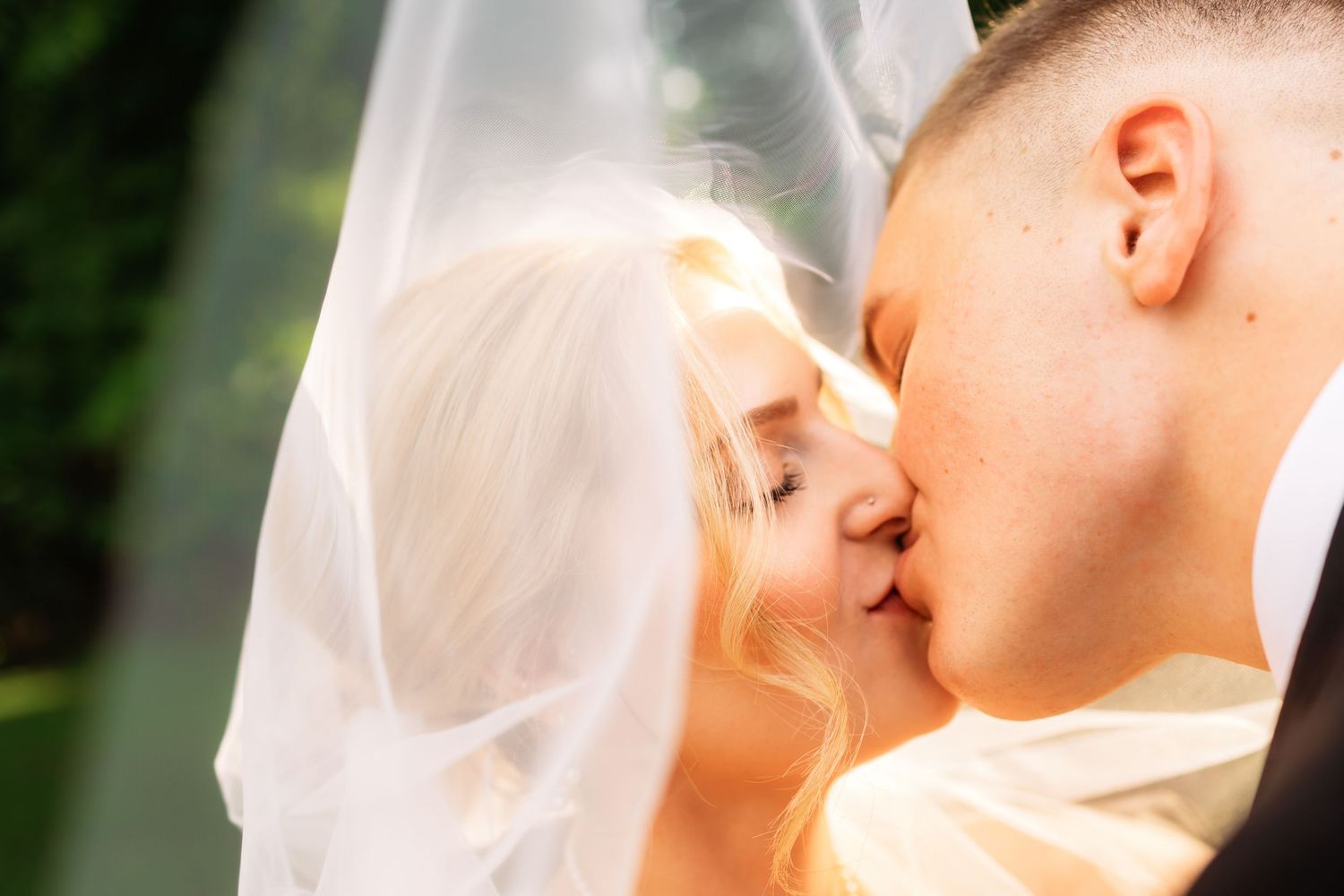 Close-up of tender wedding kiss against natural outdoor backdrop.