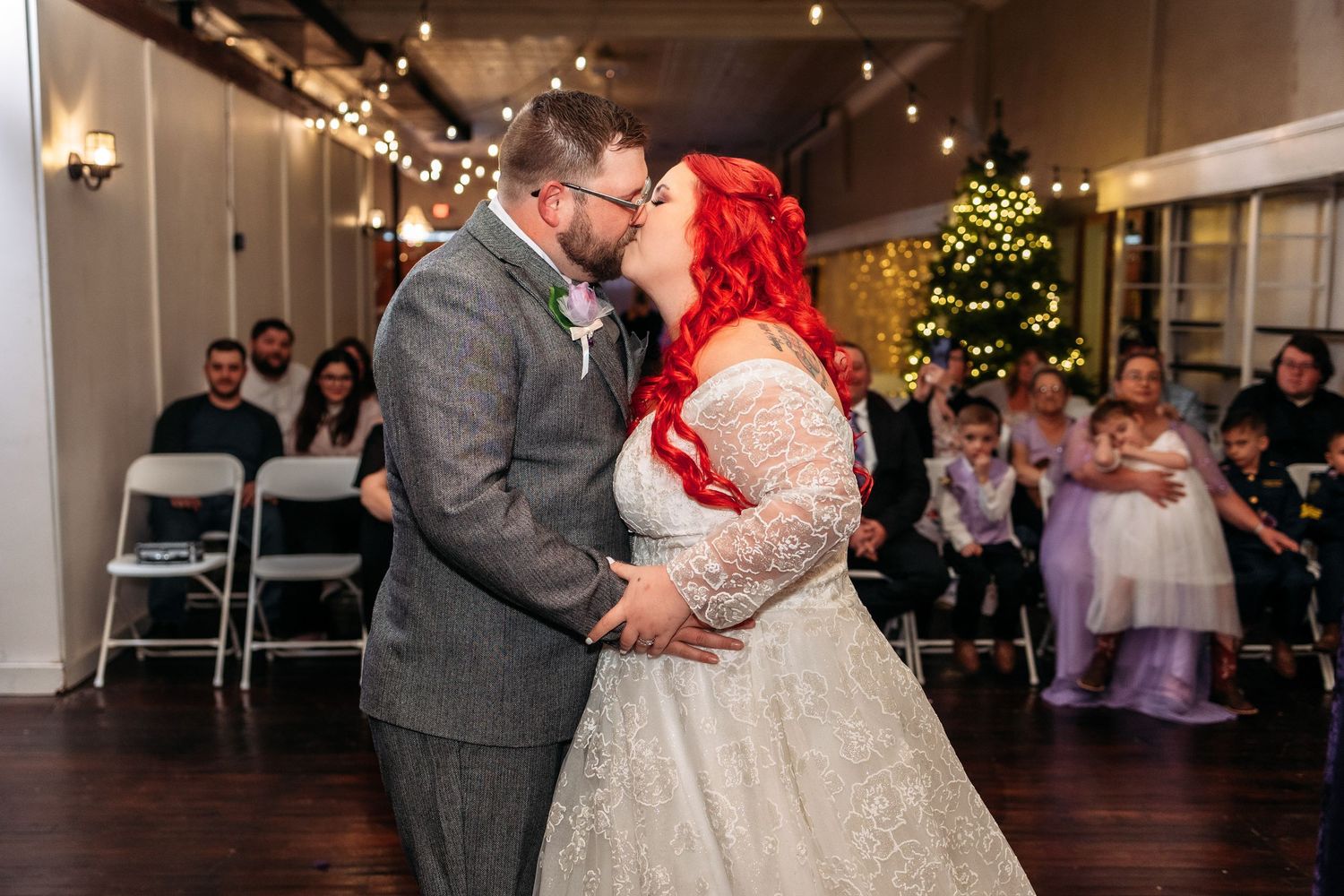 Wedding couple shares a romantic dance moment in a rustic venue decorated with Christmas lights and wreaths.