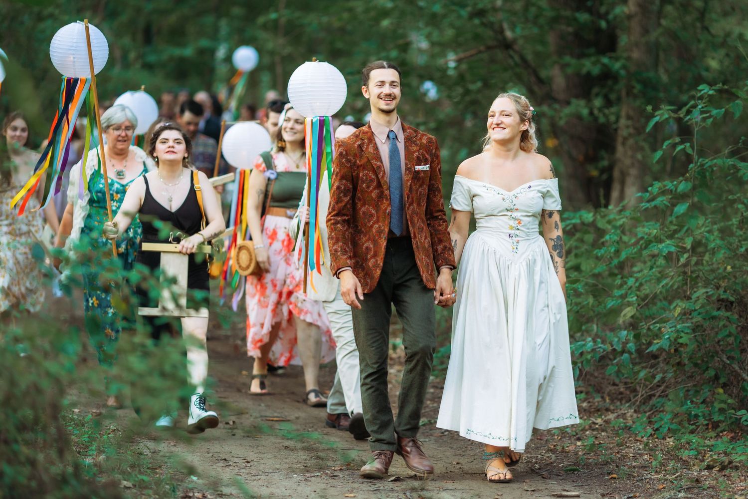 People in period costumes walk through a wooded path during an outdoor event.