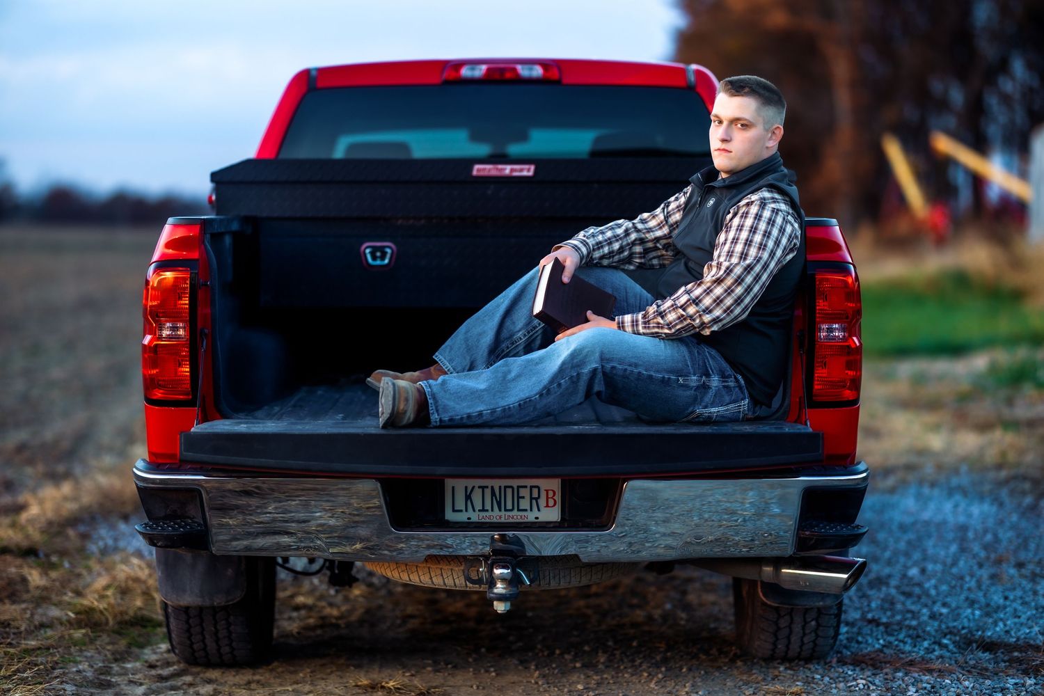 Person relaxing in the bed of a red pickup truck at sunset.