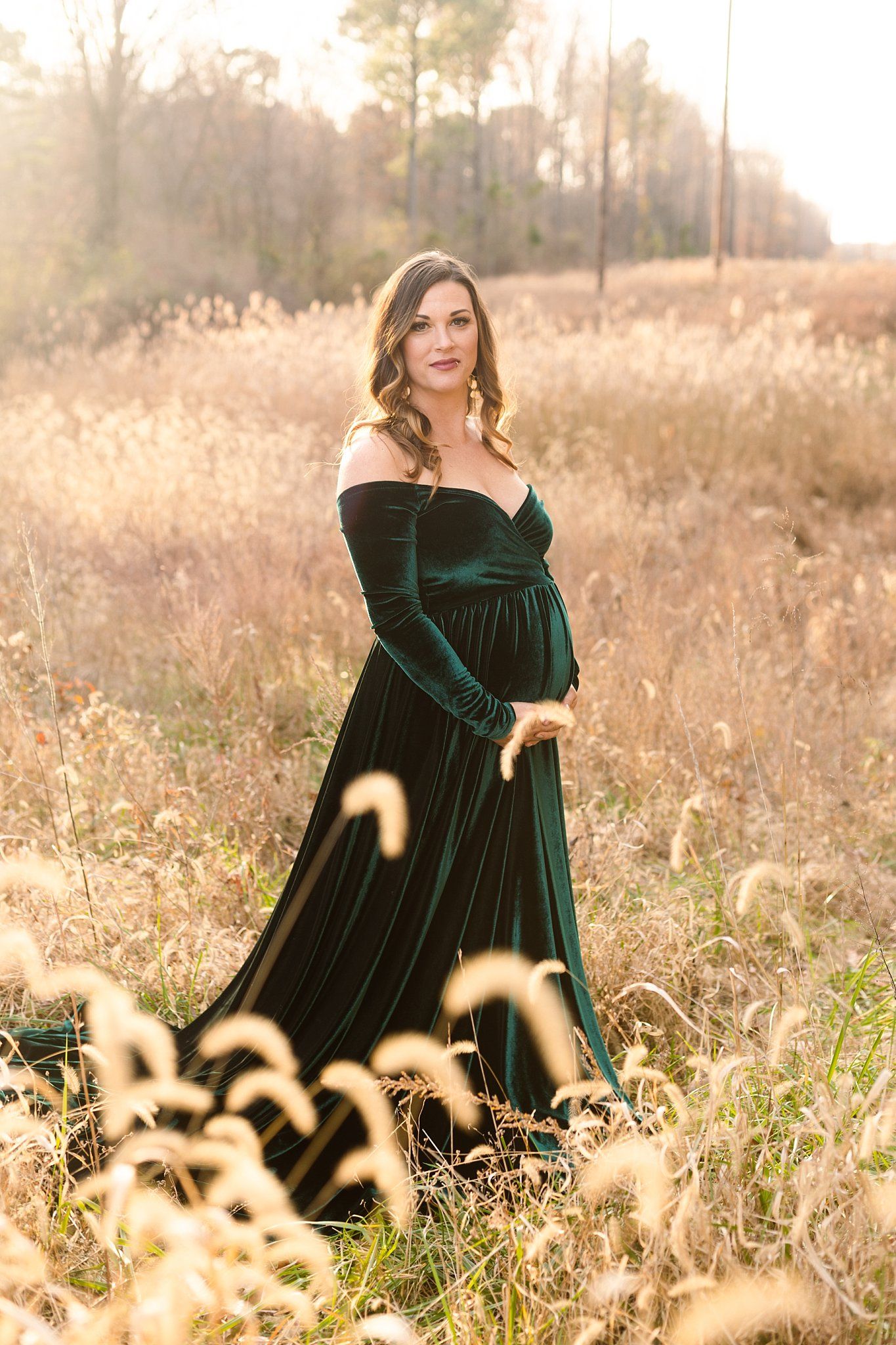Elegant maternity portrait featuring emerald velvet dress among golden autumn grasses.