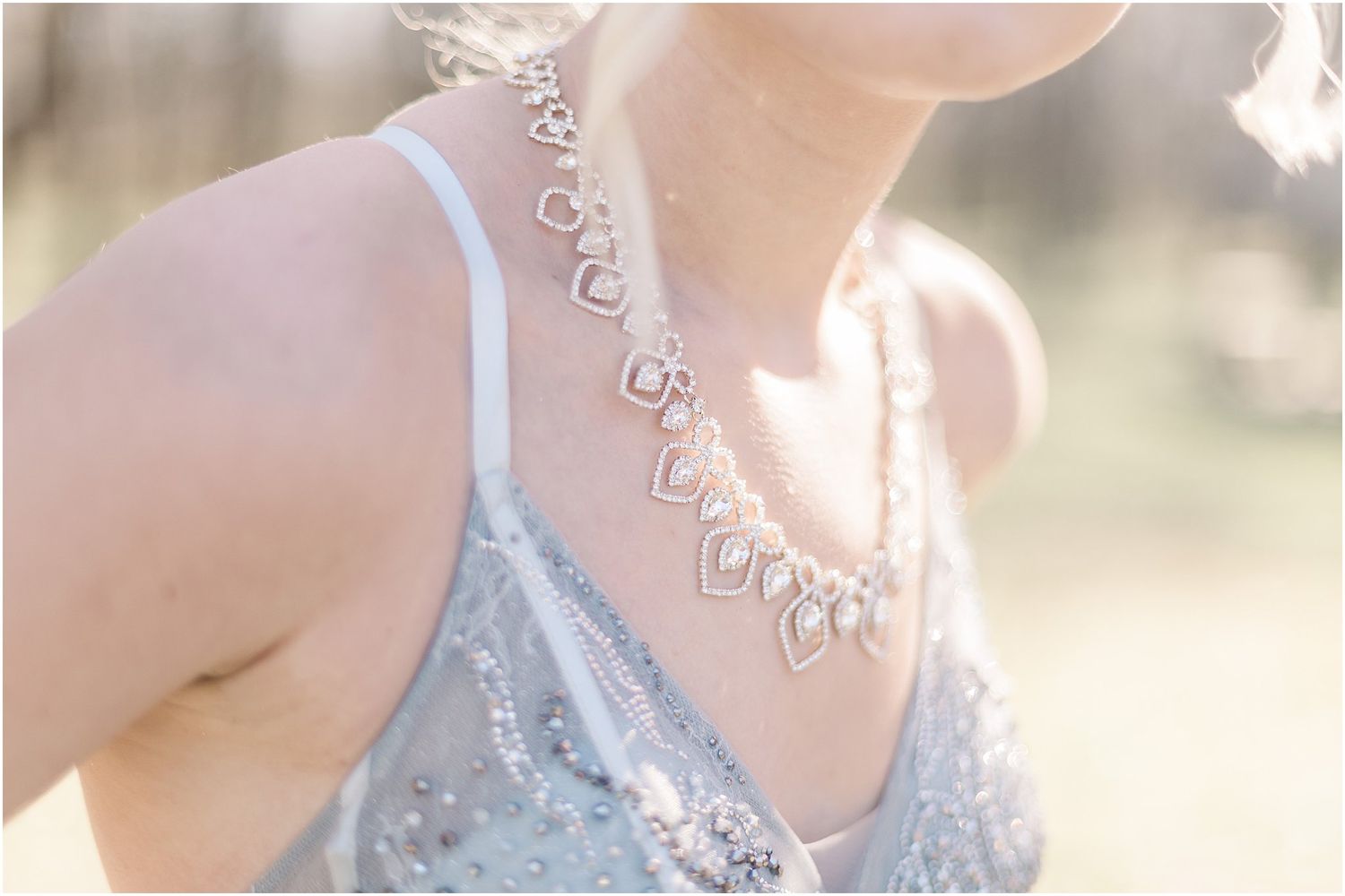 Close-up of delicate silver necklace details on light blue formal dress.