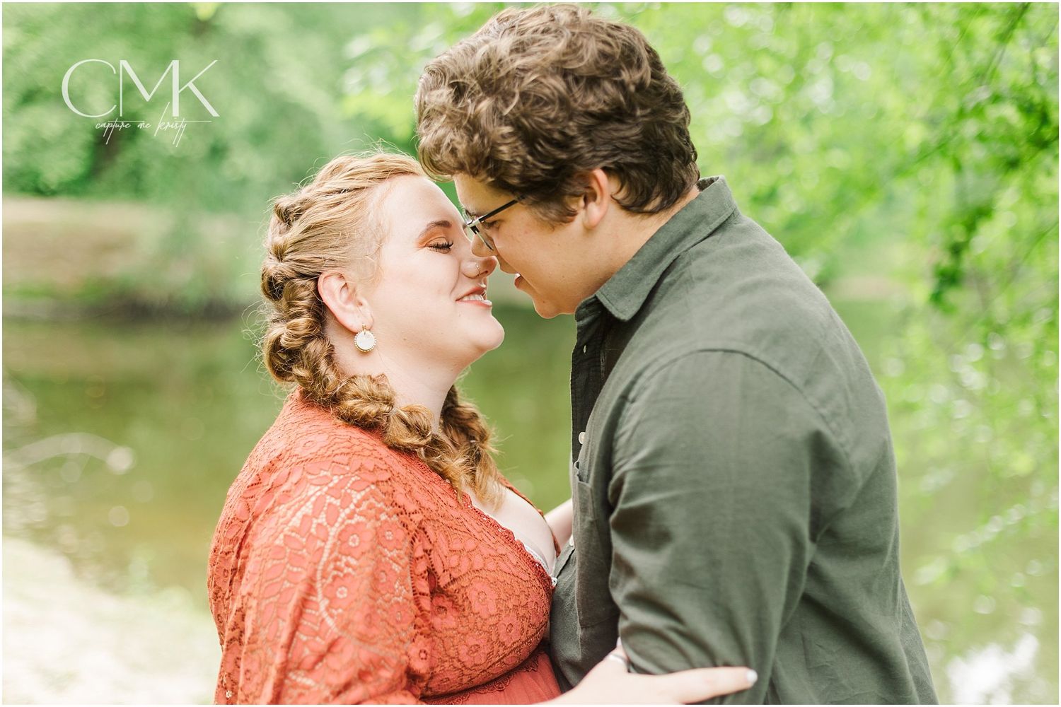 A tender moment captured between a couple in an outdoor photoshoot with a waterside backdrop.