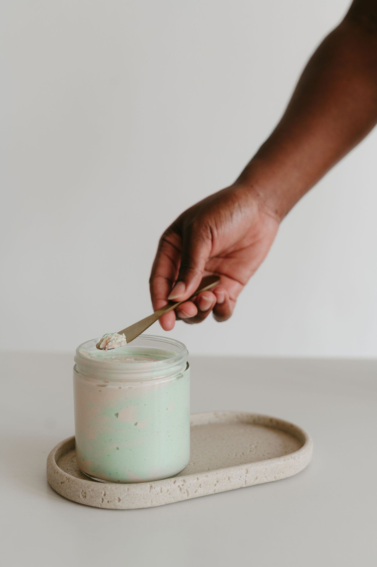 Hand scooping contents from mint green jar on ceramic plate.