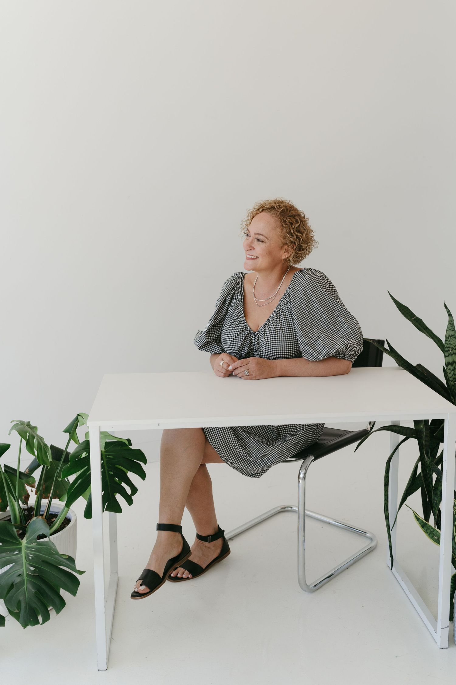 Person lying on white table with green plants in minimalist setting.