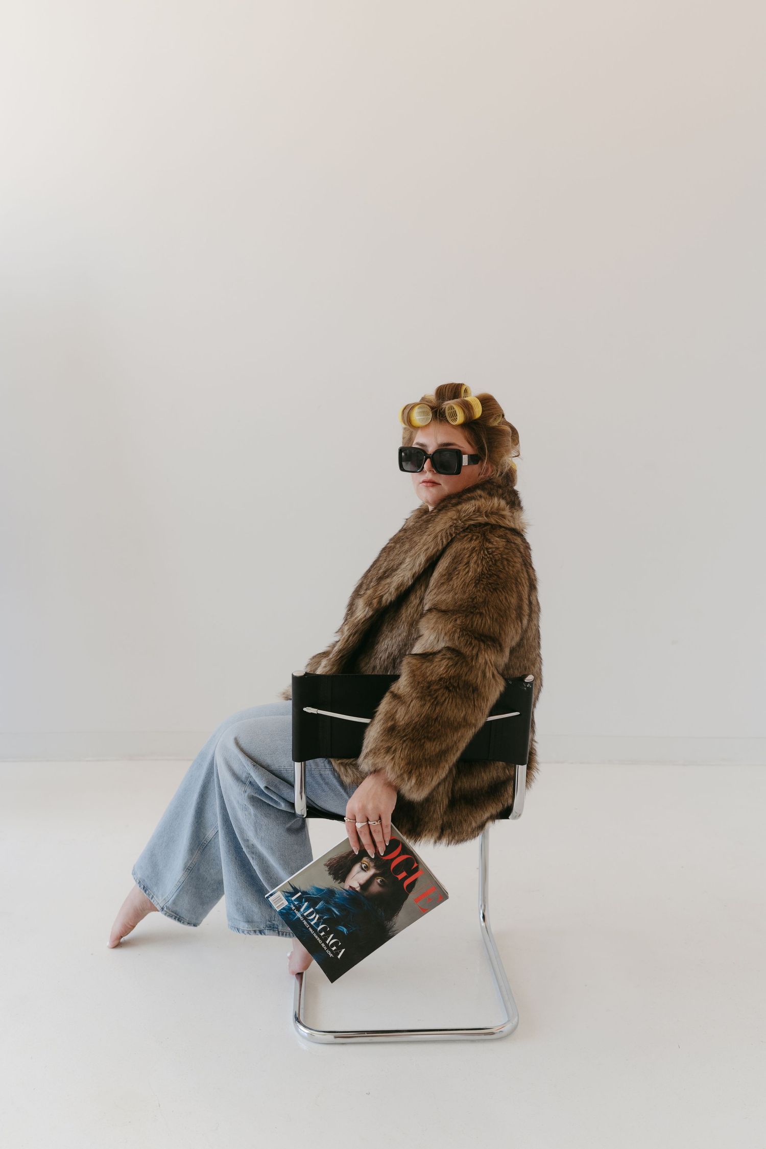 Lifestyle photos of person in fur coat and sunglasses lounging on modern chair.