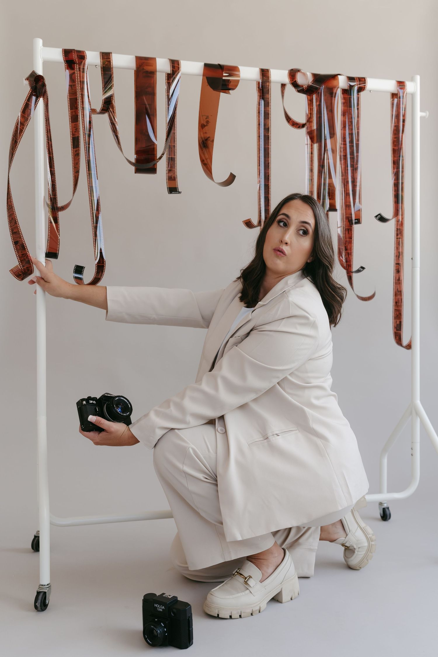 Model in white outfit poses playfully with leather straps hanging from ceiling in studio setting.