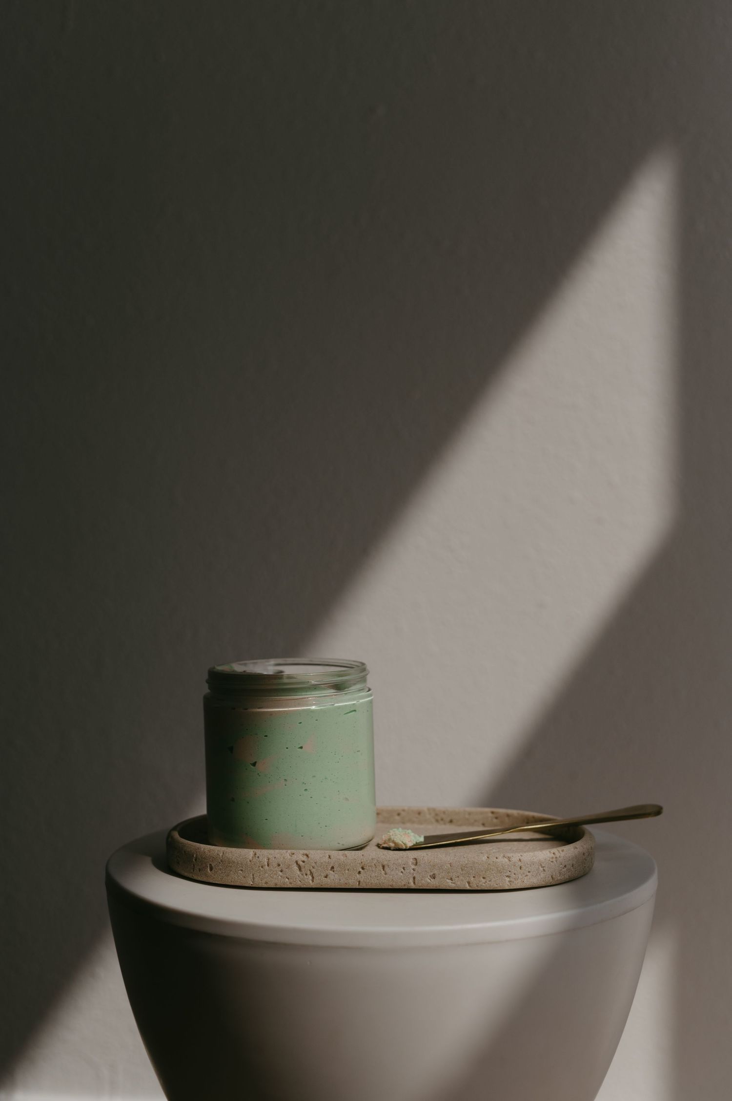 Mint green jar on ceramic plate with dramatic diagonal lighting.