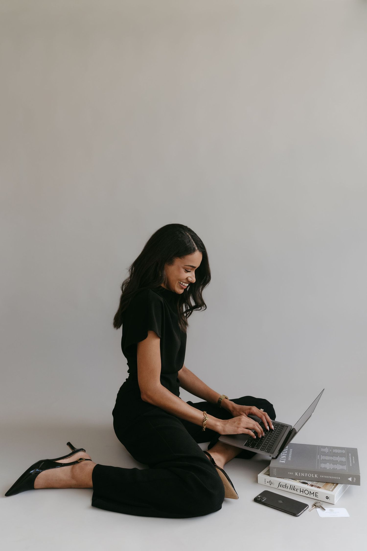 Businesswoman in black outfit working on laptop while sitting on floor with books and materials.