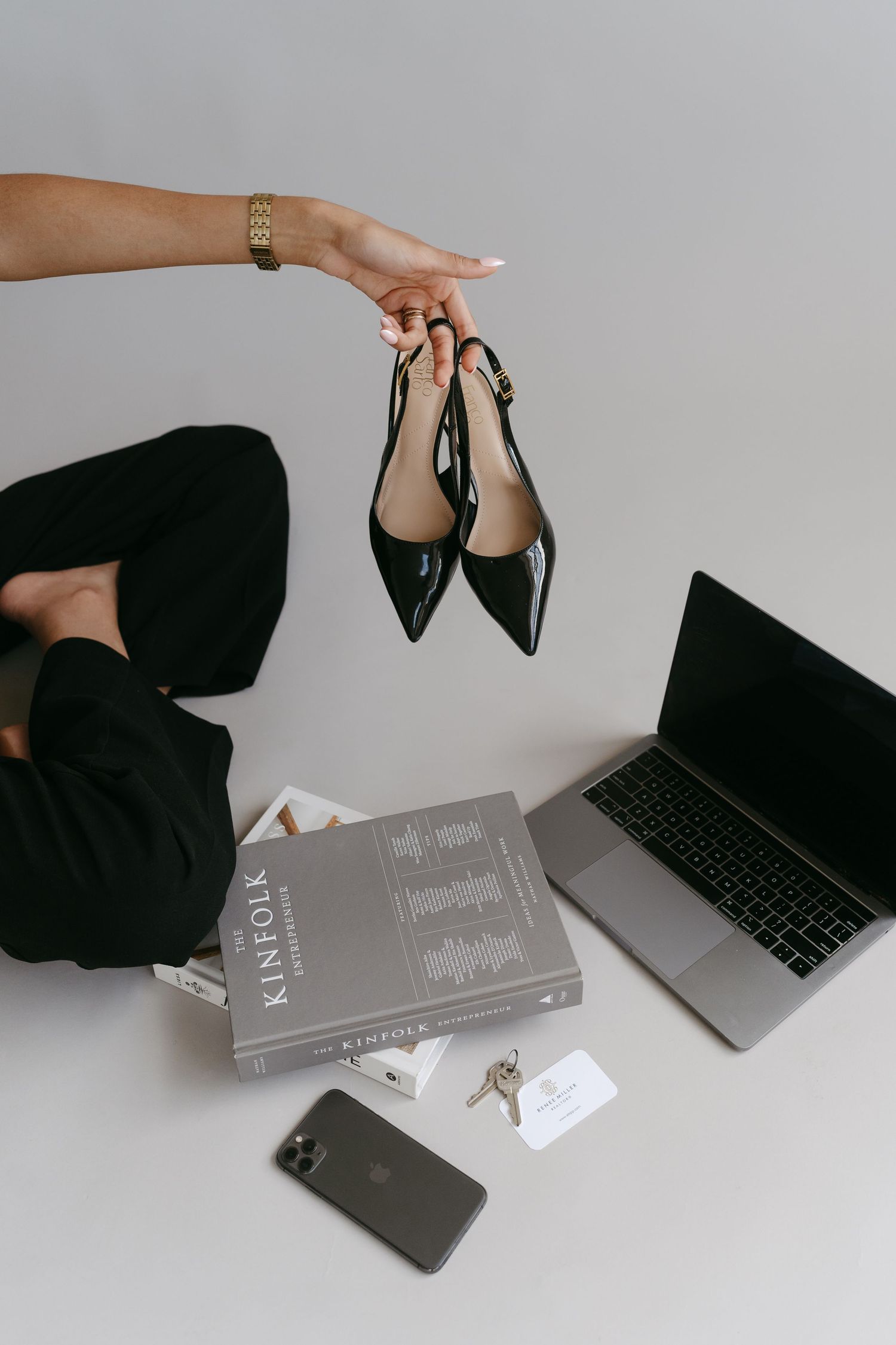 Flat lay styling with laptop, books, phone and black heels against white background.