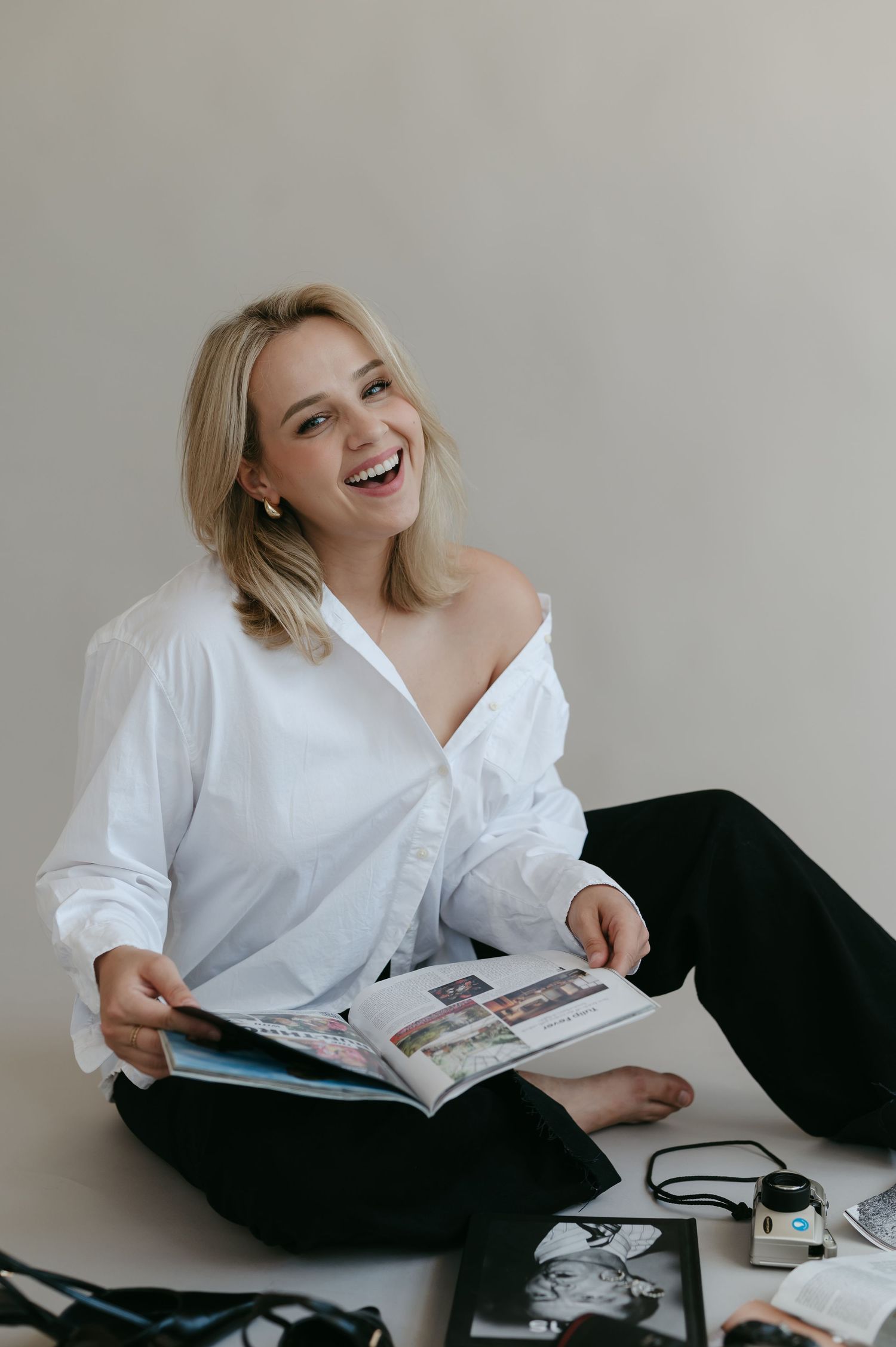 Person in white shirt lounges with magazine on dark furniture against light background.