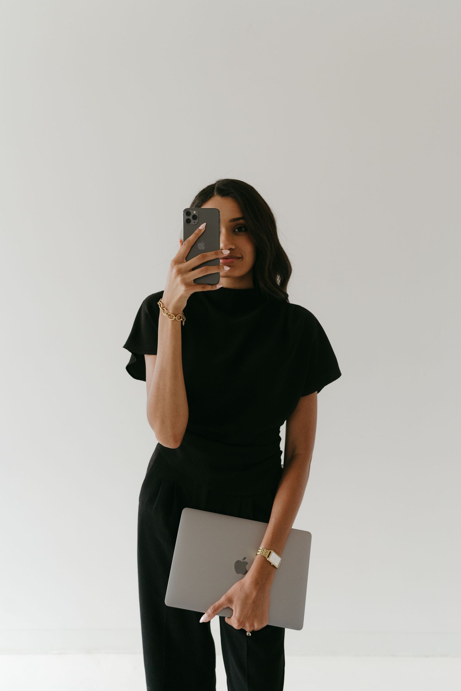 Professional lifestyle photoshoot featuring a person in black holding a laptop against a white background.