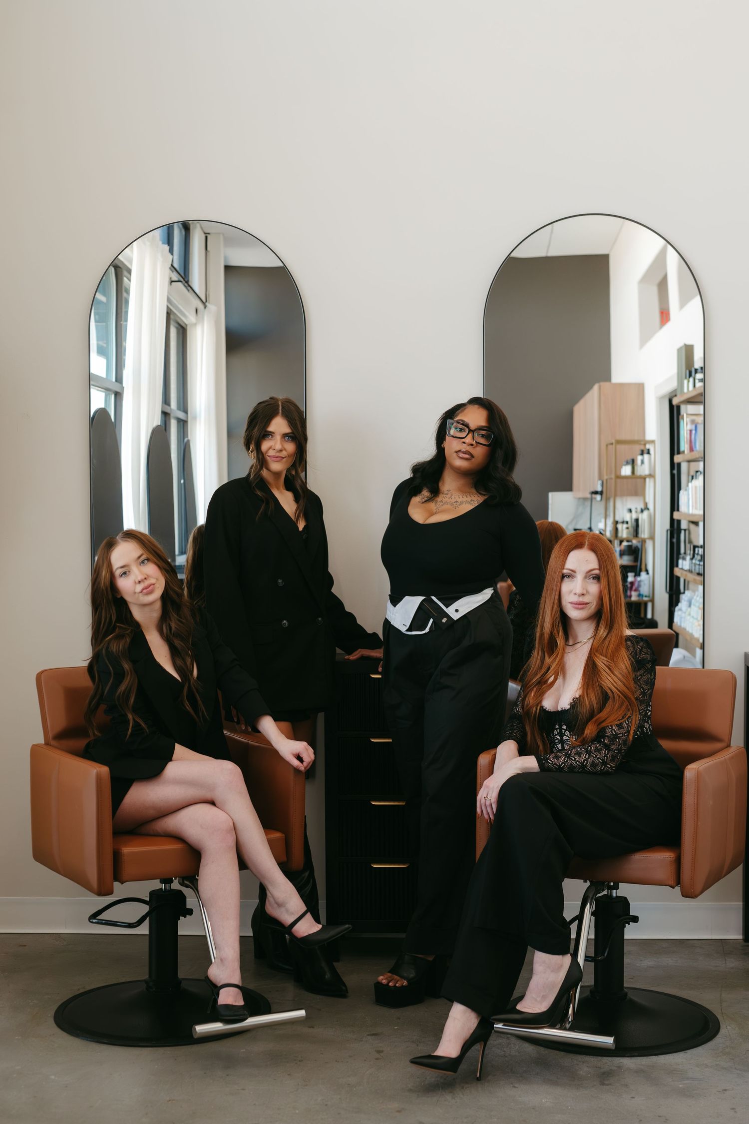 A series of five connected photos showing a group in black outfits posing on brown leather chairs in a white room.