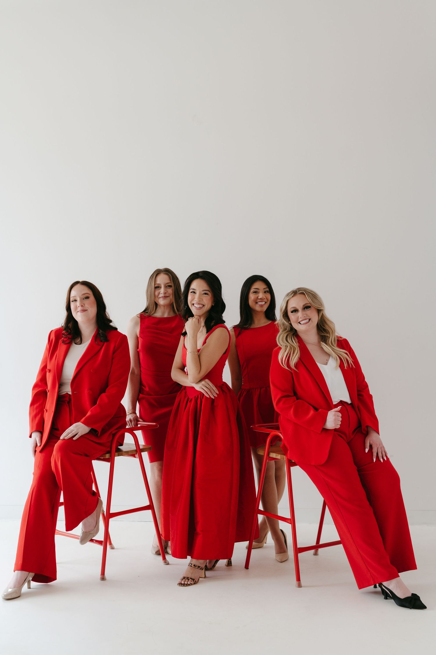 A group of people in matching red outfits pose together with red chairs in a minimalist white studio setting.