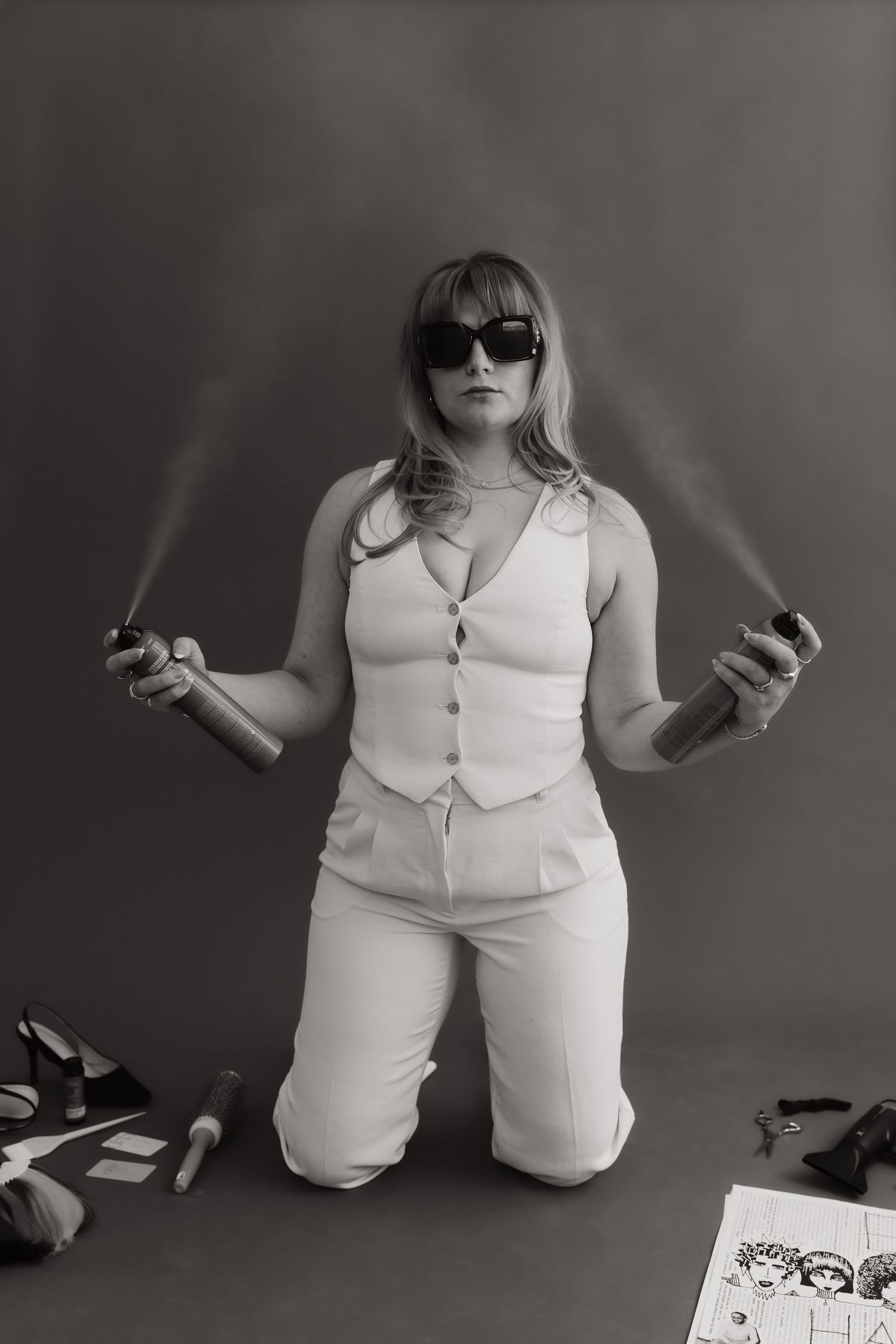 Person in white vest and pants holding spray bottles in dramatic black and white portrait.