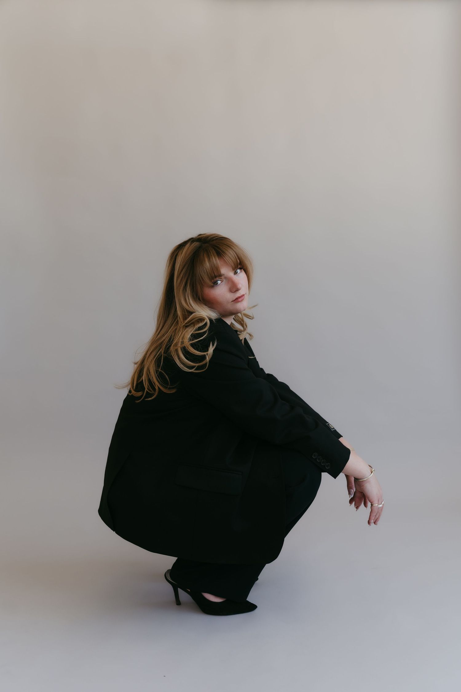 Figure in black outfit crouching in artistic pose against white studio backdrop.