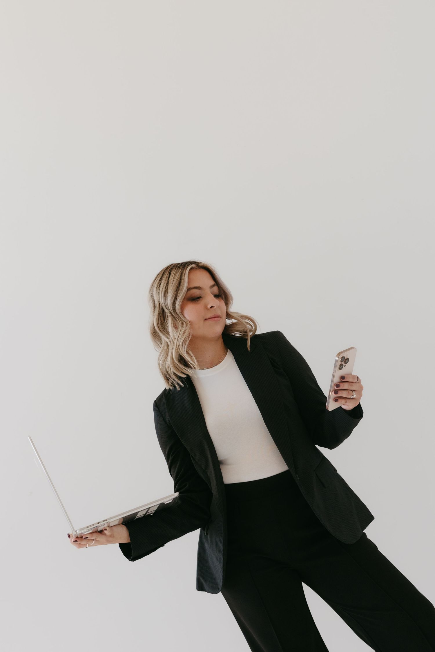 Fashion model in black blazer and white top poses dynamically against light background in editorial series.