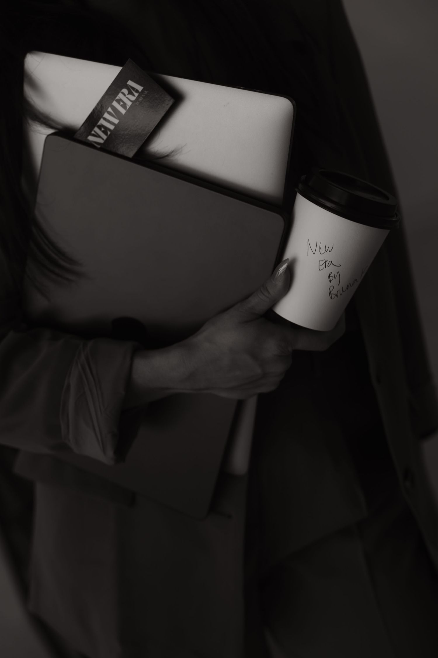 Black and white photo of a person holding a laptop, folder, and coffee cup with handwritten notes.