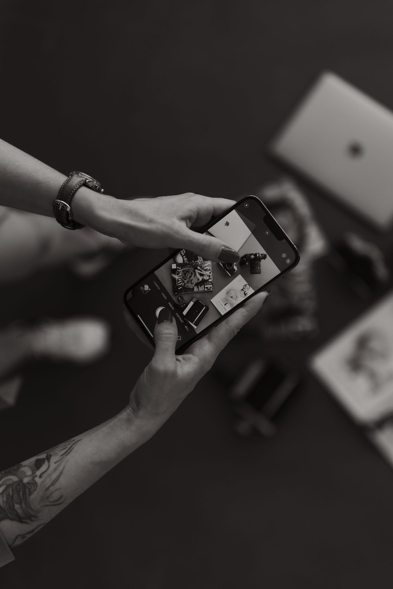 Hands holding smartphone in dark setting showing black and white images.