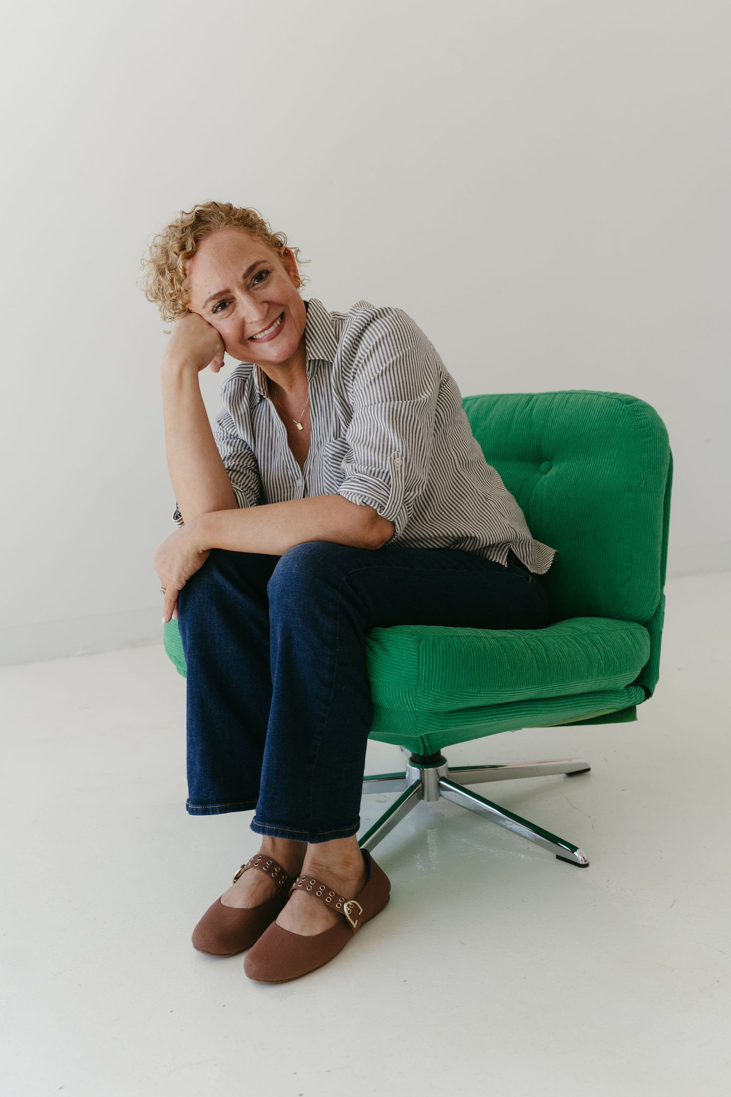 Person lounging on a bright green modern chair in casual attire against white backdrop.
