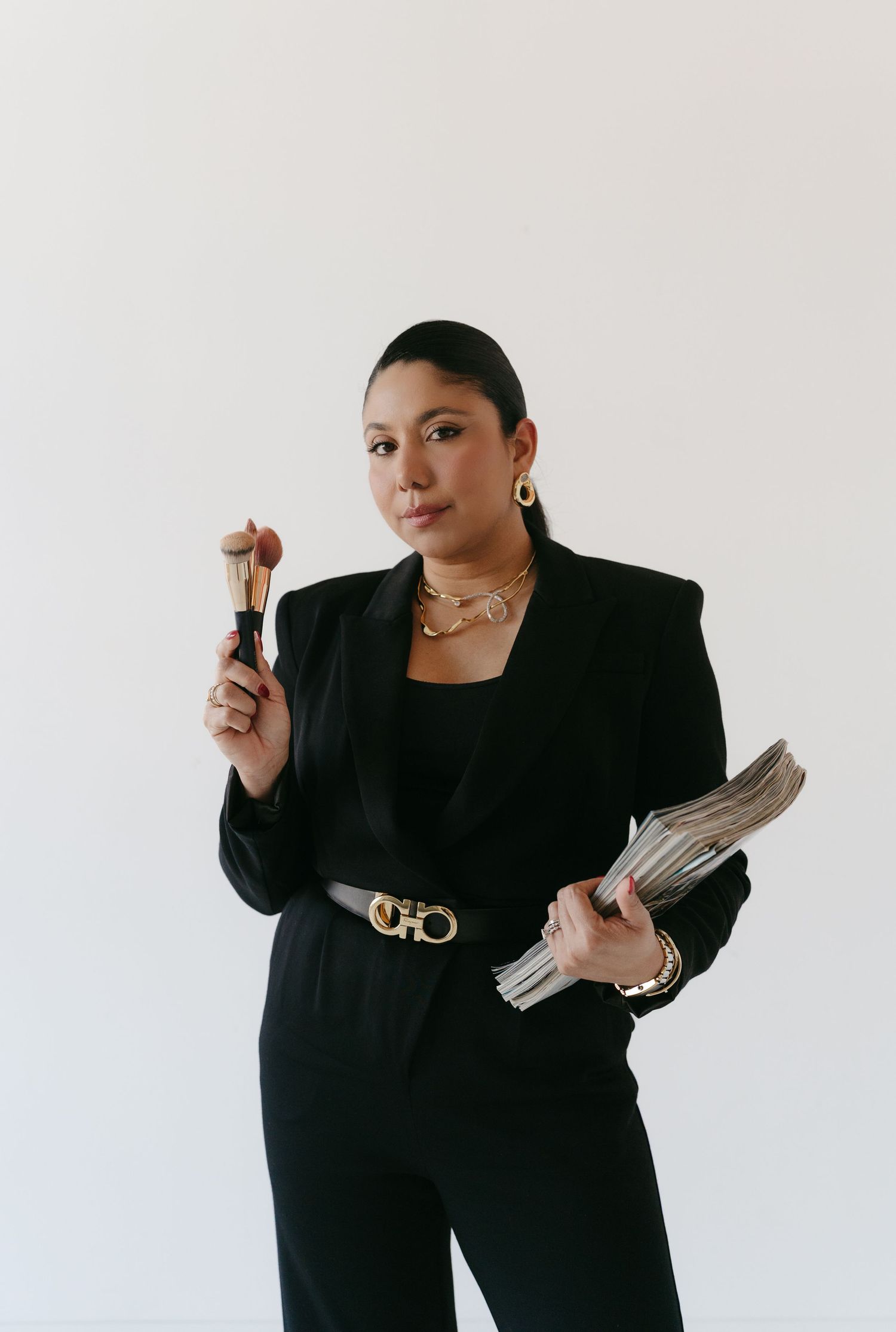 Professional in all-black outfit poses confidently with documents against white background.